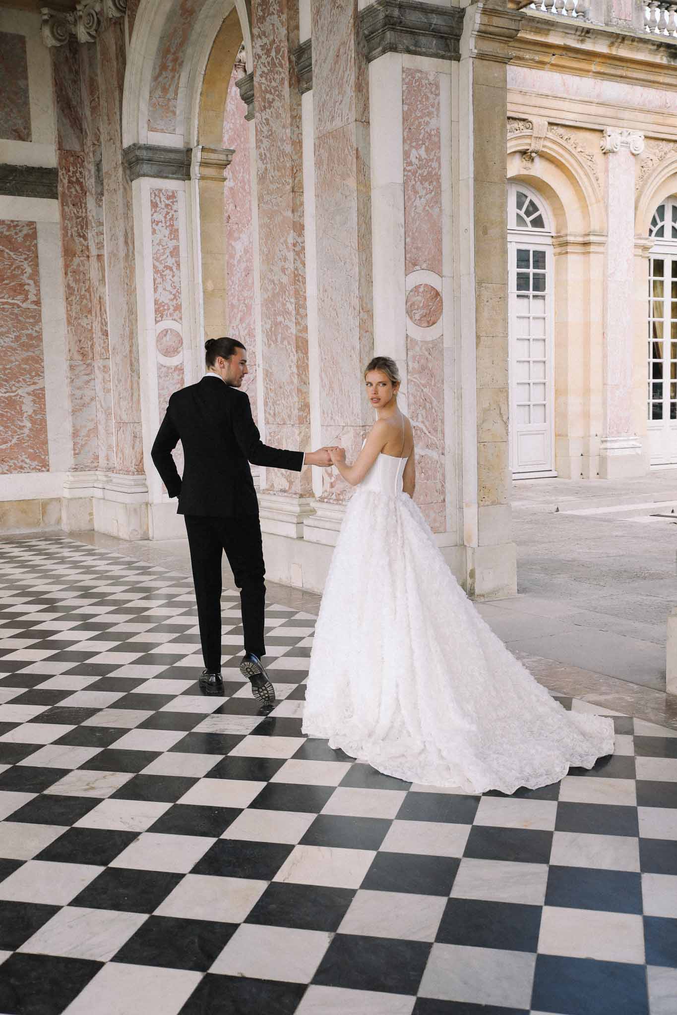 Bride and groom formal portrait in classical European palace corridor with marble columns
