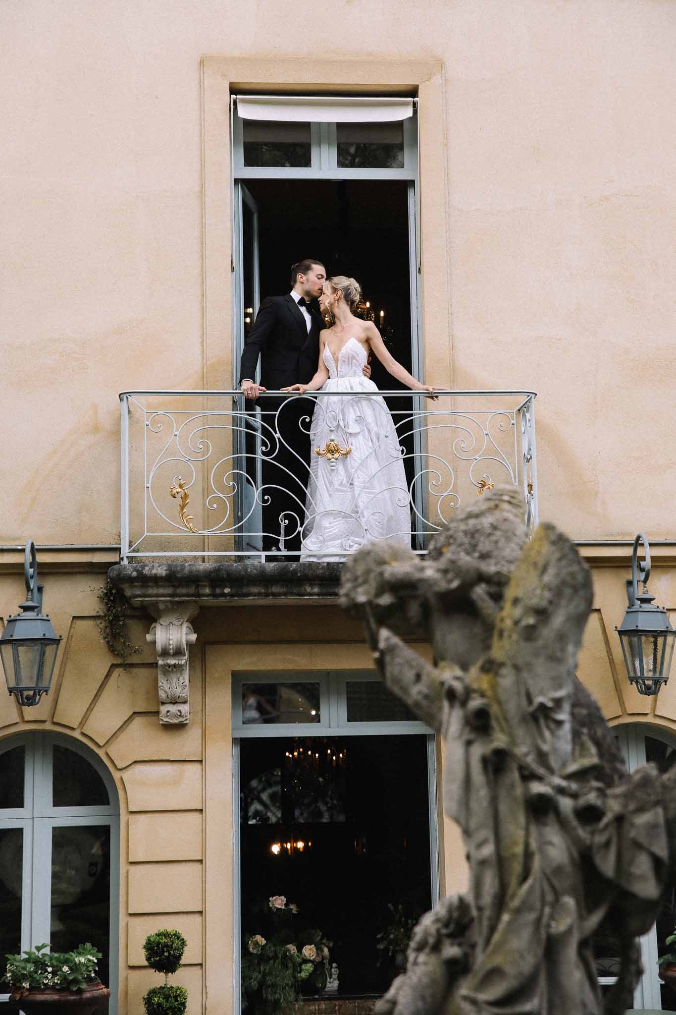 Bride and groom kiss on ornate balcony at classical château estate