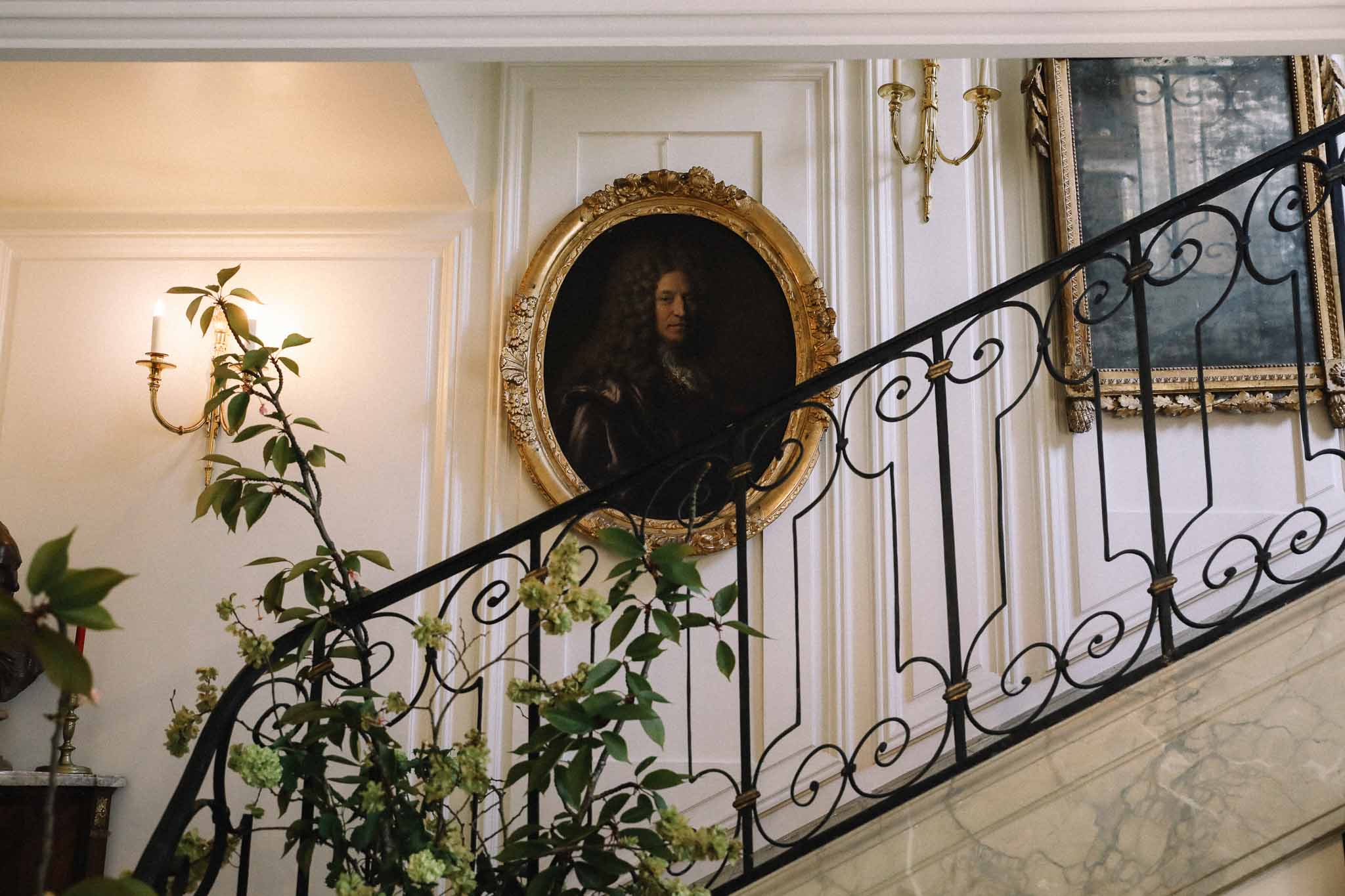 Elegant classical staircase with wrought-iron railing and greenery at French wedding venue interior