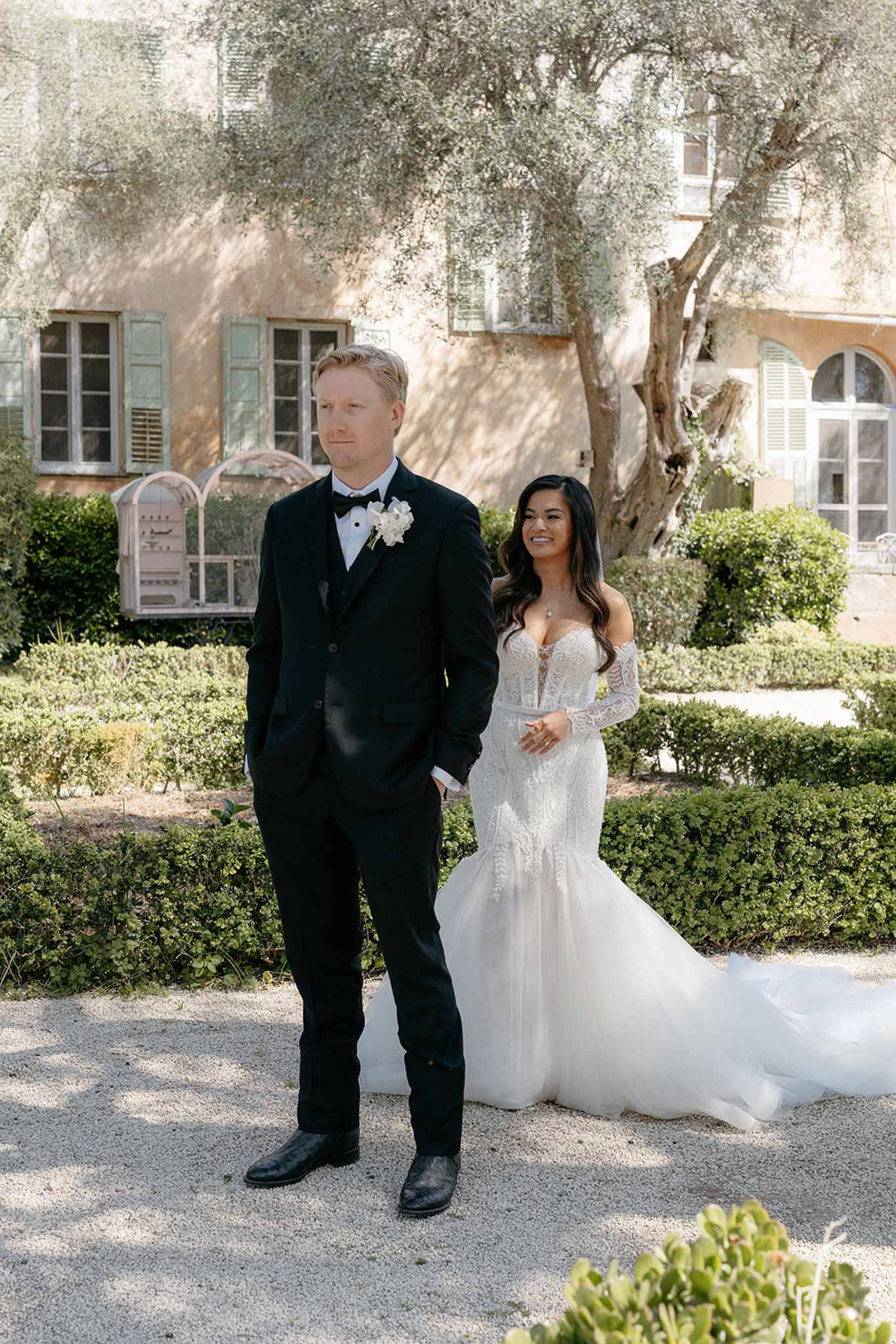 Bride and groom posing in a Provencal manor garden with olive tree and ochre-walled backdrop