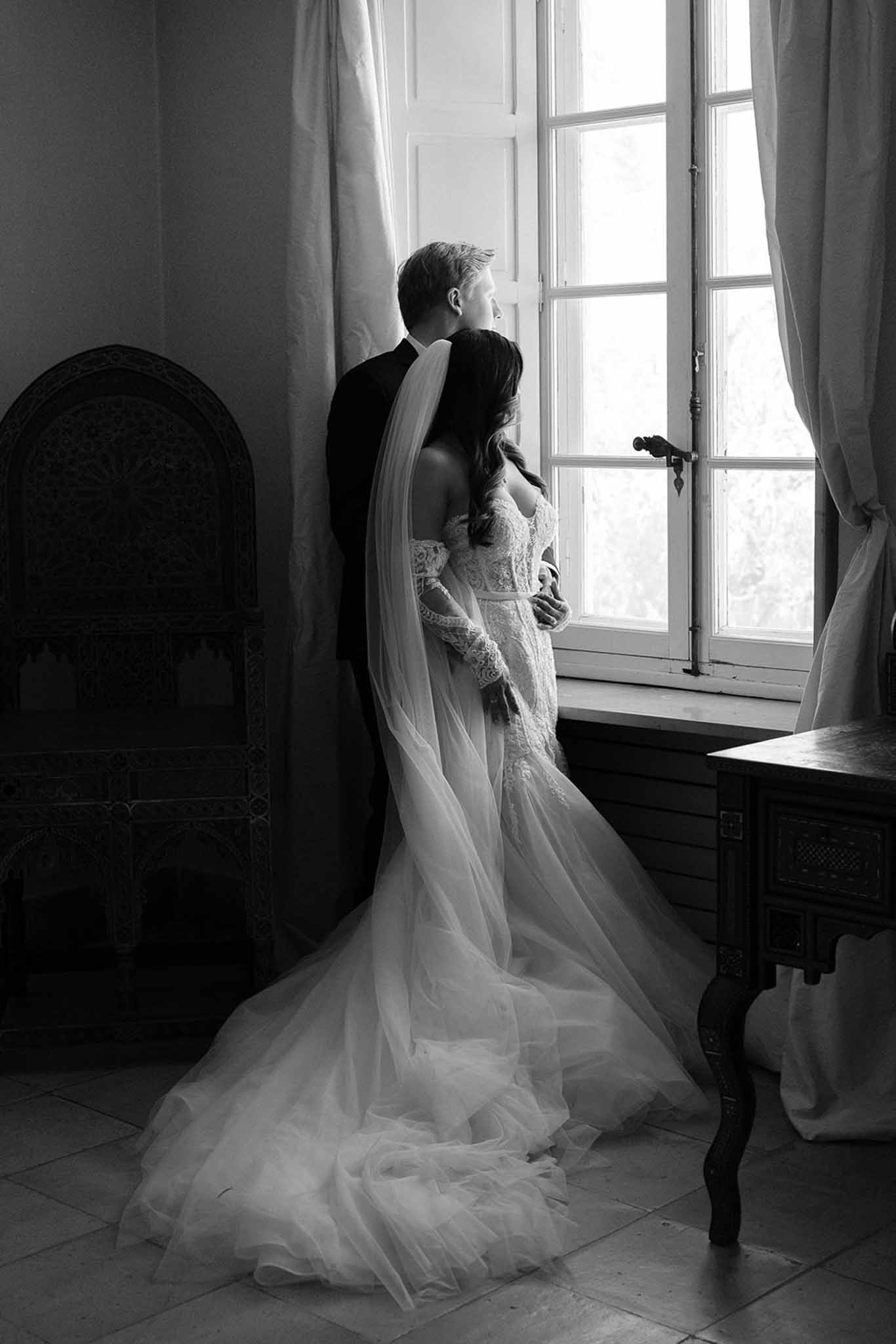 Black and white portrait of bride and groom embracing at open French window in Moorish-style interior