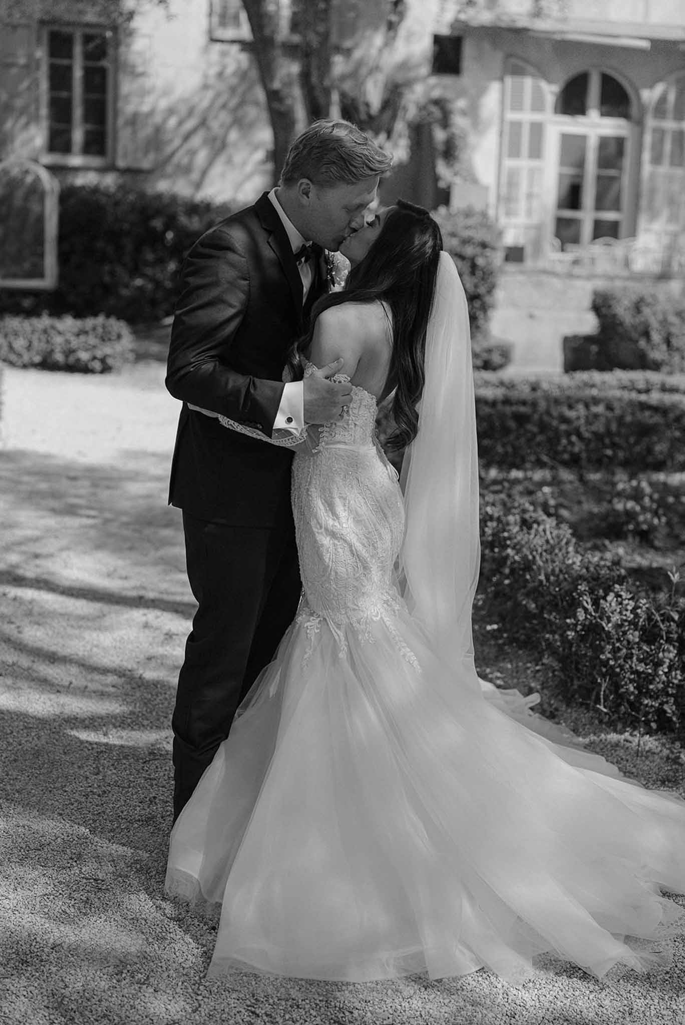 Black and white kiss in formal hedgerow garden with bride in lace mermaid gown and cathedral veil