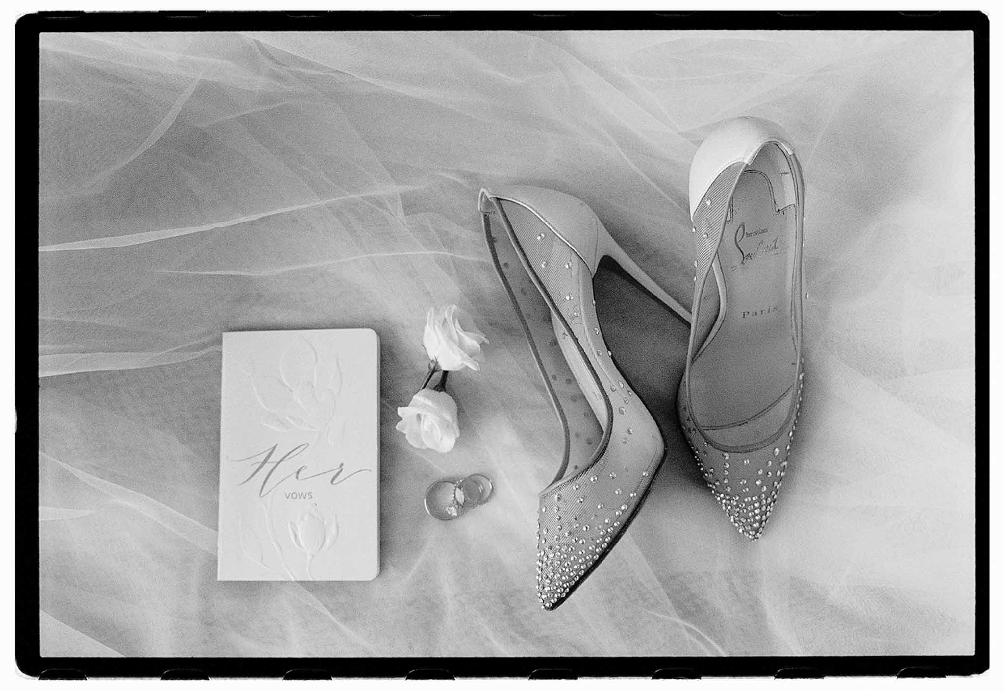 Crystal Louboutin pumps, vow booklet, wedding bands, and rose blooms on tulle veil in B&W