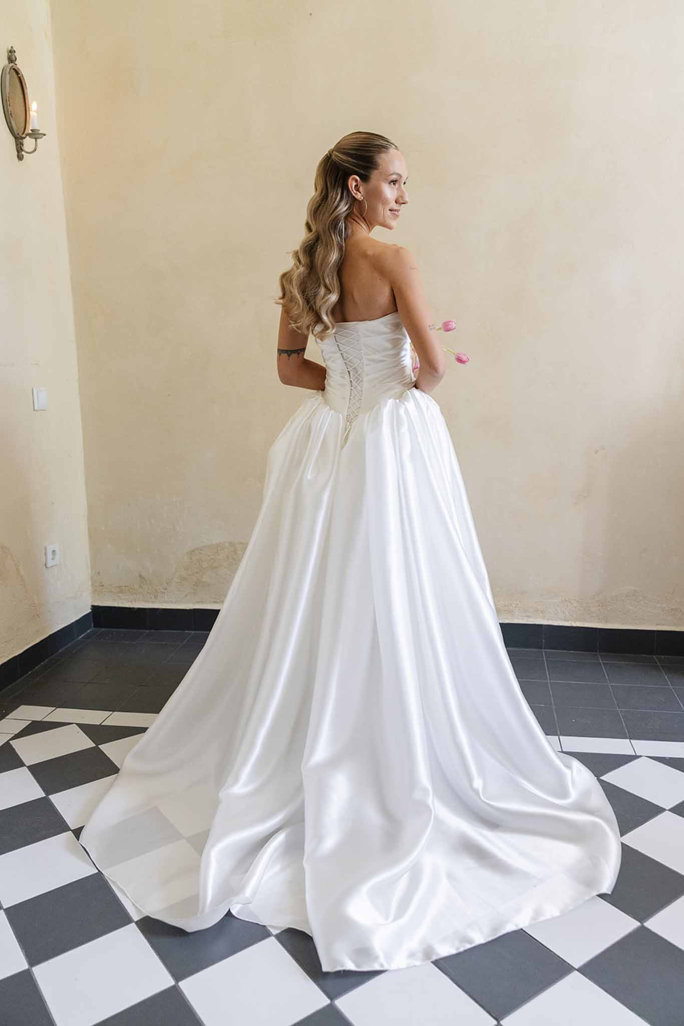 Bride in ivory ballgown with laced corset back holding pink bouquet in interior room with diamond tile floor