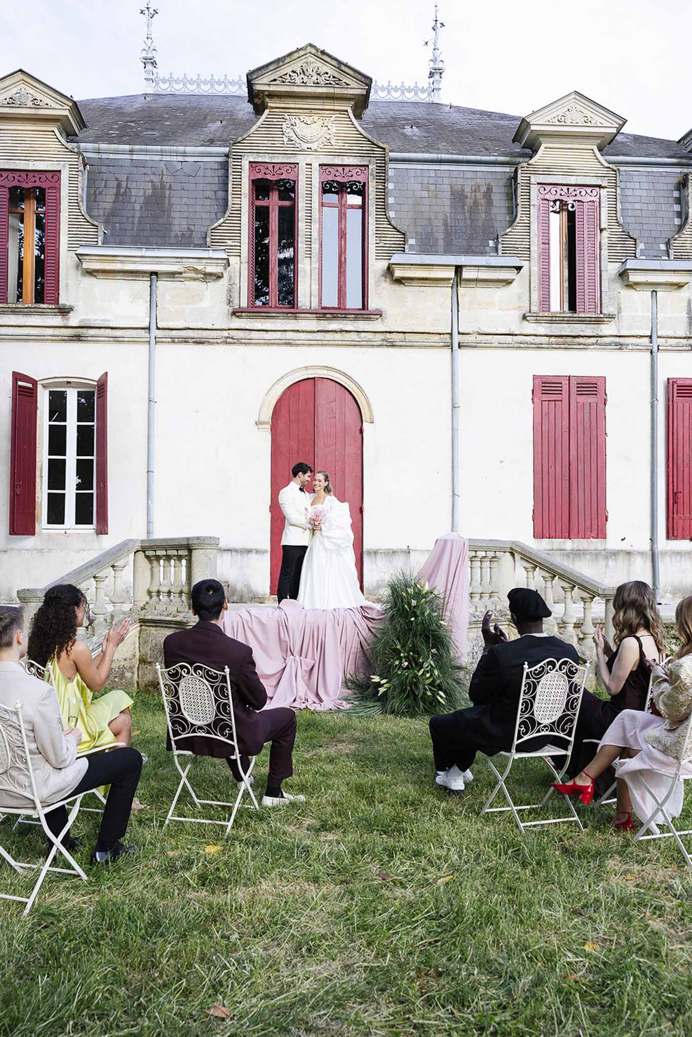 Outdoor wedding ceremony on lawn in front of historic white building with burgundy shutters