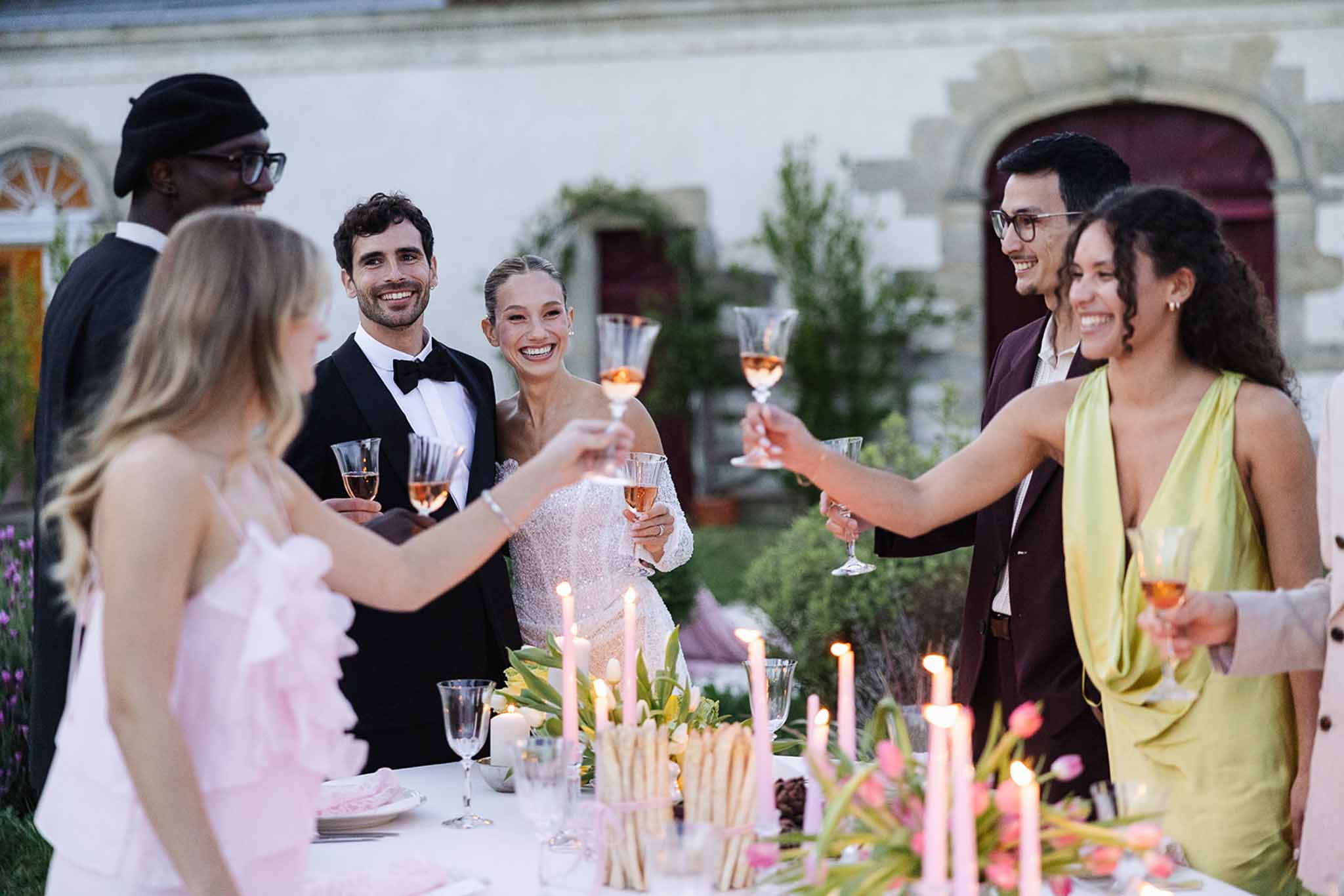 Bride and groom toasting with guests during reception on Mediterranean terrace with candlelit table setting