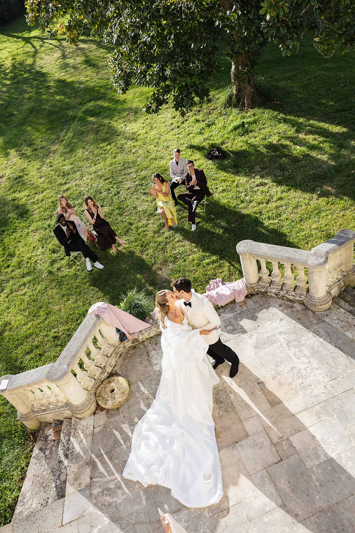 Bride and groom on stone terrace with wedding guests on lawn at chateau grounds