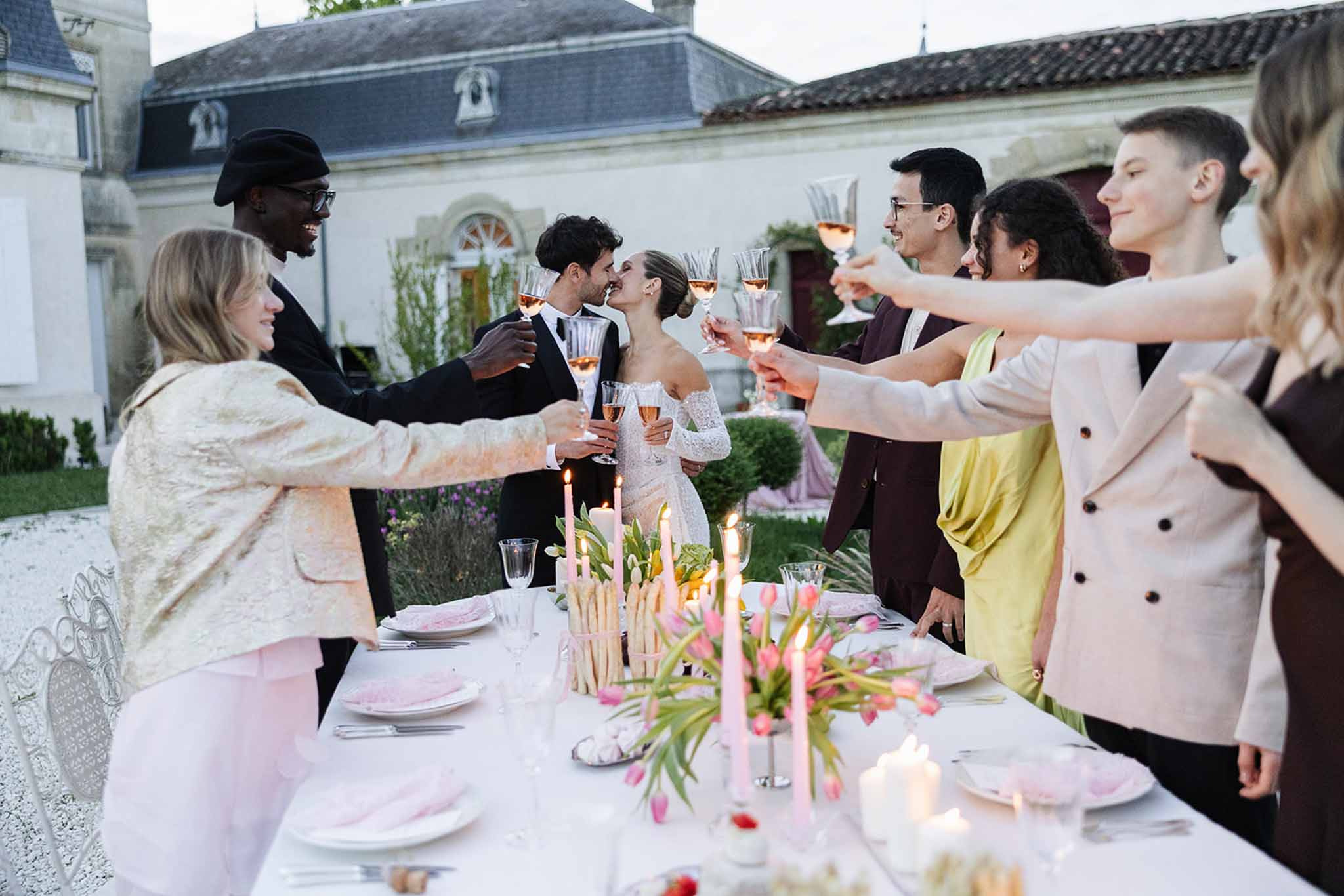 Guests raising rose champagne coupes at table with pink tulip centrepieces and blush plates