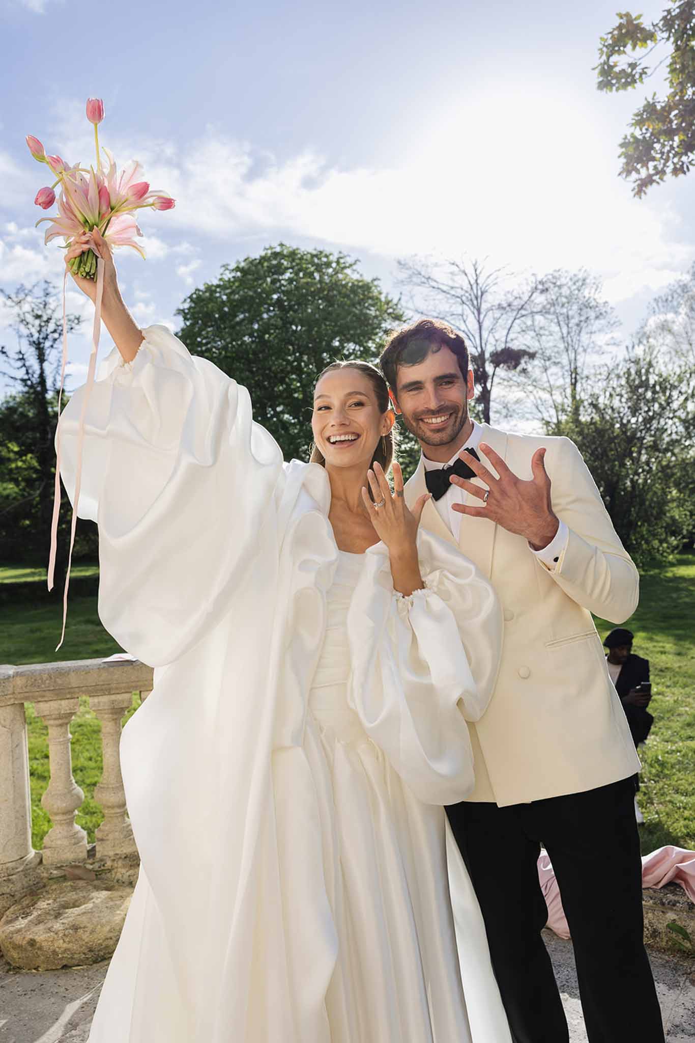 Bride and groom celebrating together in formal garden with coral amaryllis bouquet