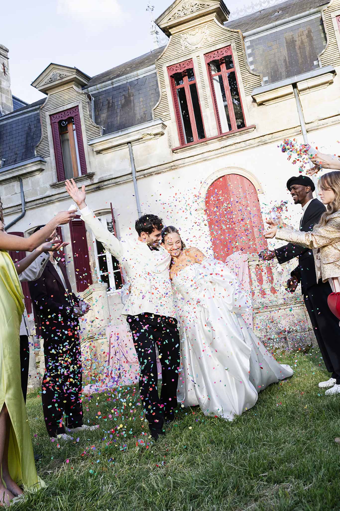 Bride and groom exit ceremony under confetti shower at historic stone building courtyard