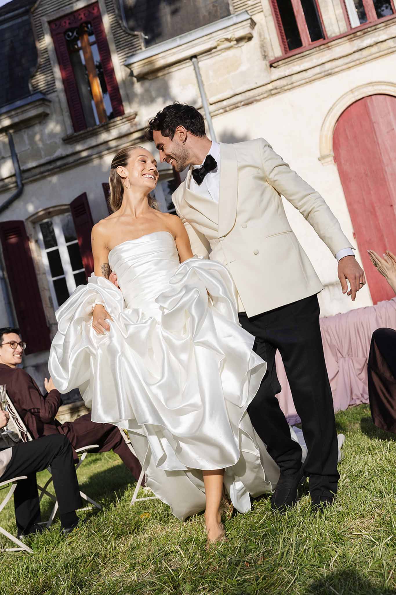Bride and groom sharing joyful moment in courtyard of historic stone building with burgundy shutters