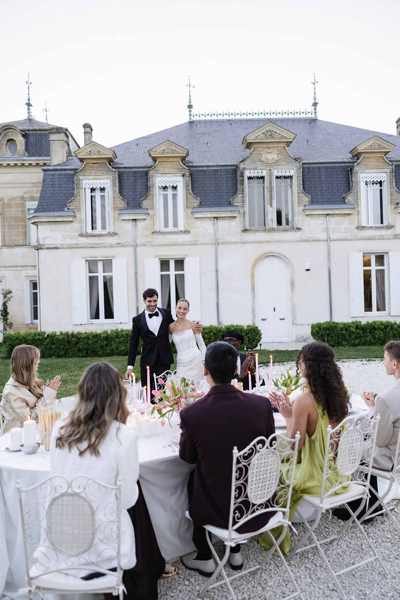 Bride and groom walking through outdoor reception at French château with guests dining at elegant white tables