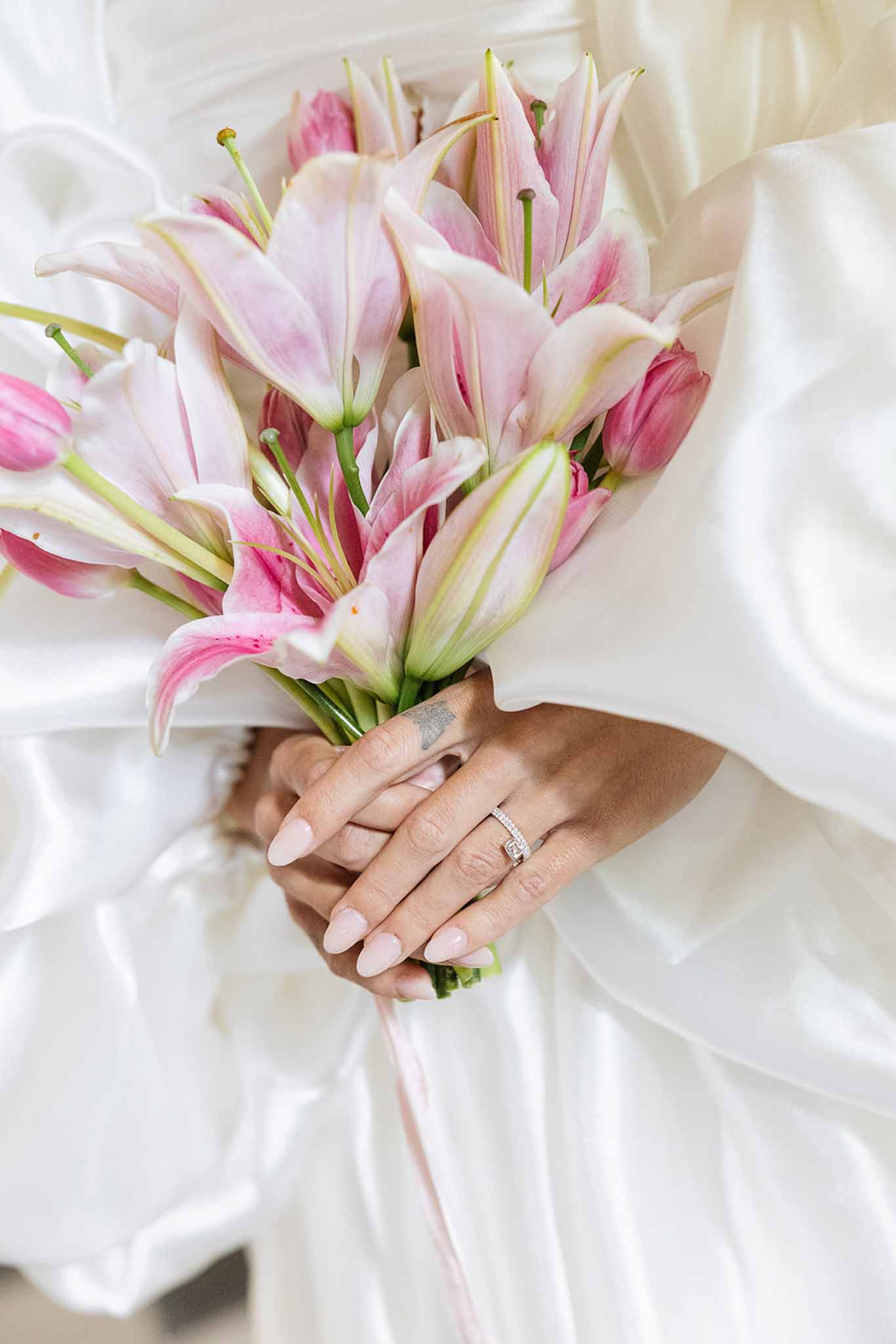 Bride holding pink and white lily bouquet with diamond rings at wedding
