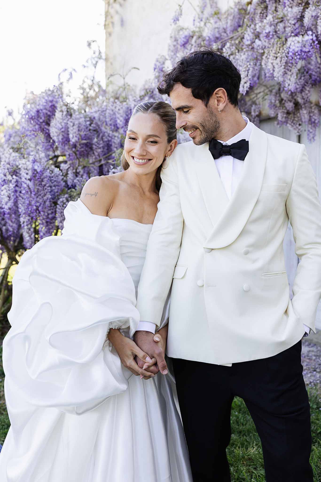 Bride and groom intimate portrait surrounded by purple wisteria blooms in garden setting