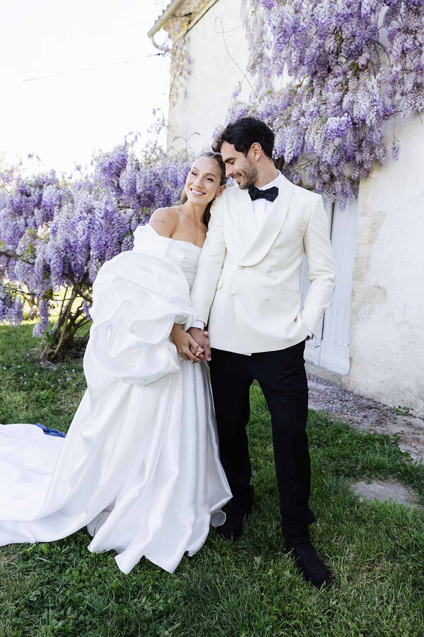 Couple portrait against purple wisteria-covered stone wall in garden setting