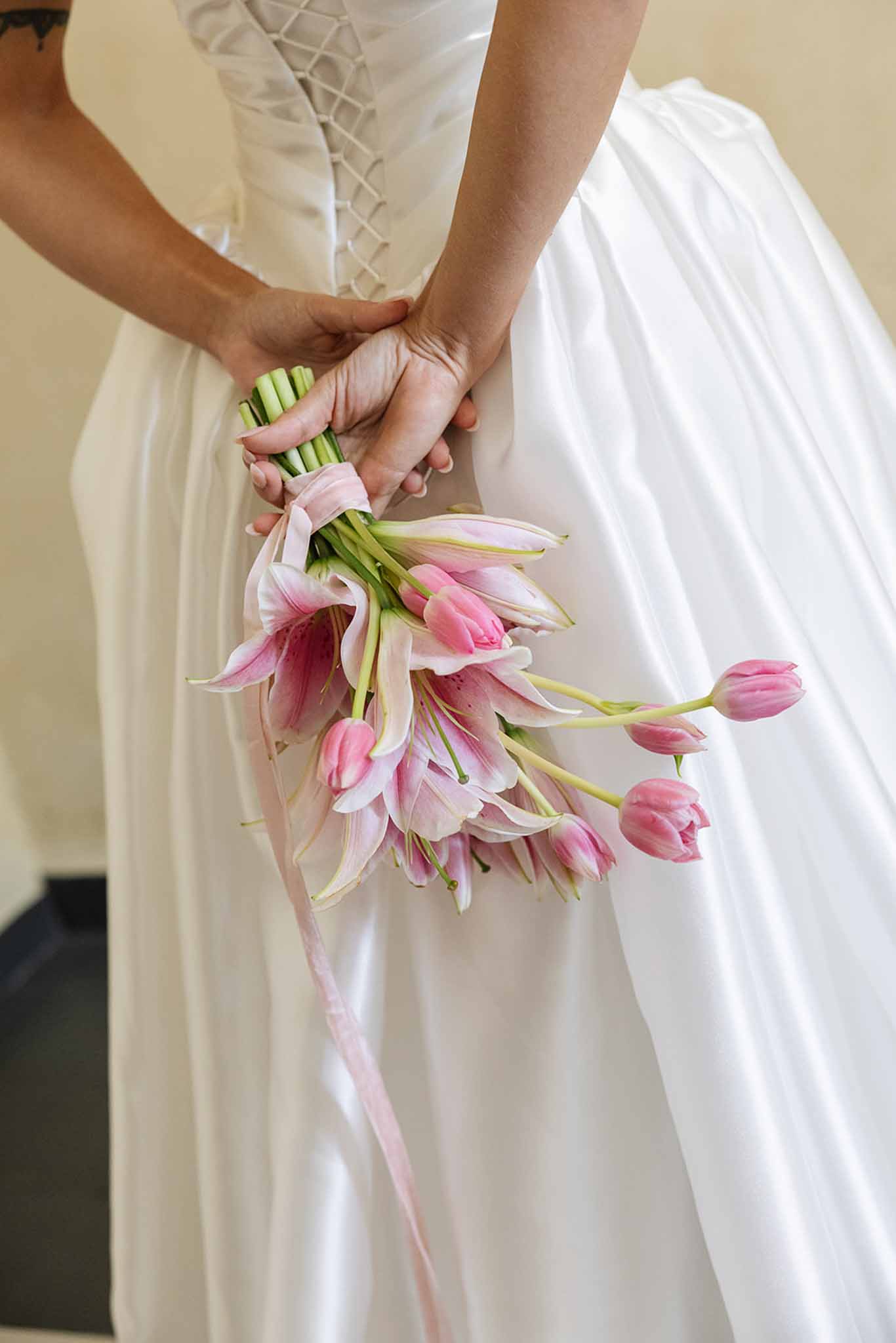 Bride holding pink and white tulip bouquet in ivory corset wedding dress indoors