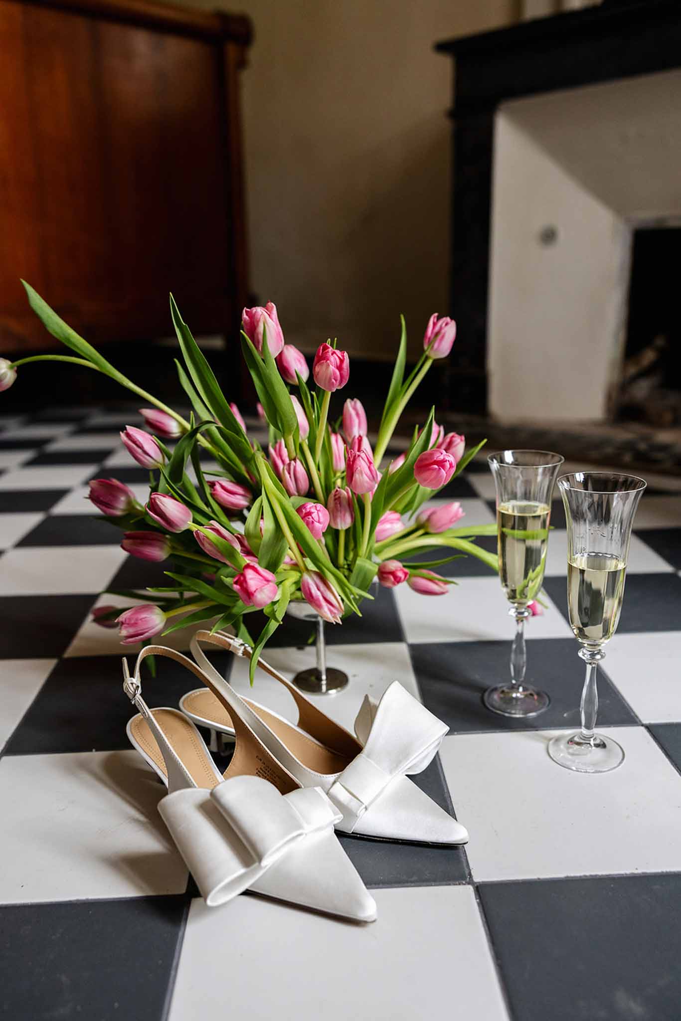 Ivory bridal heels and pink tulips arranged on checkerboard floor in getting ready space