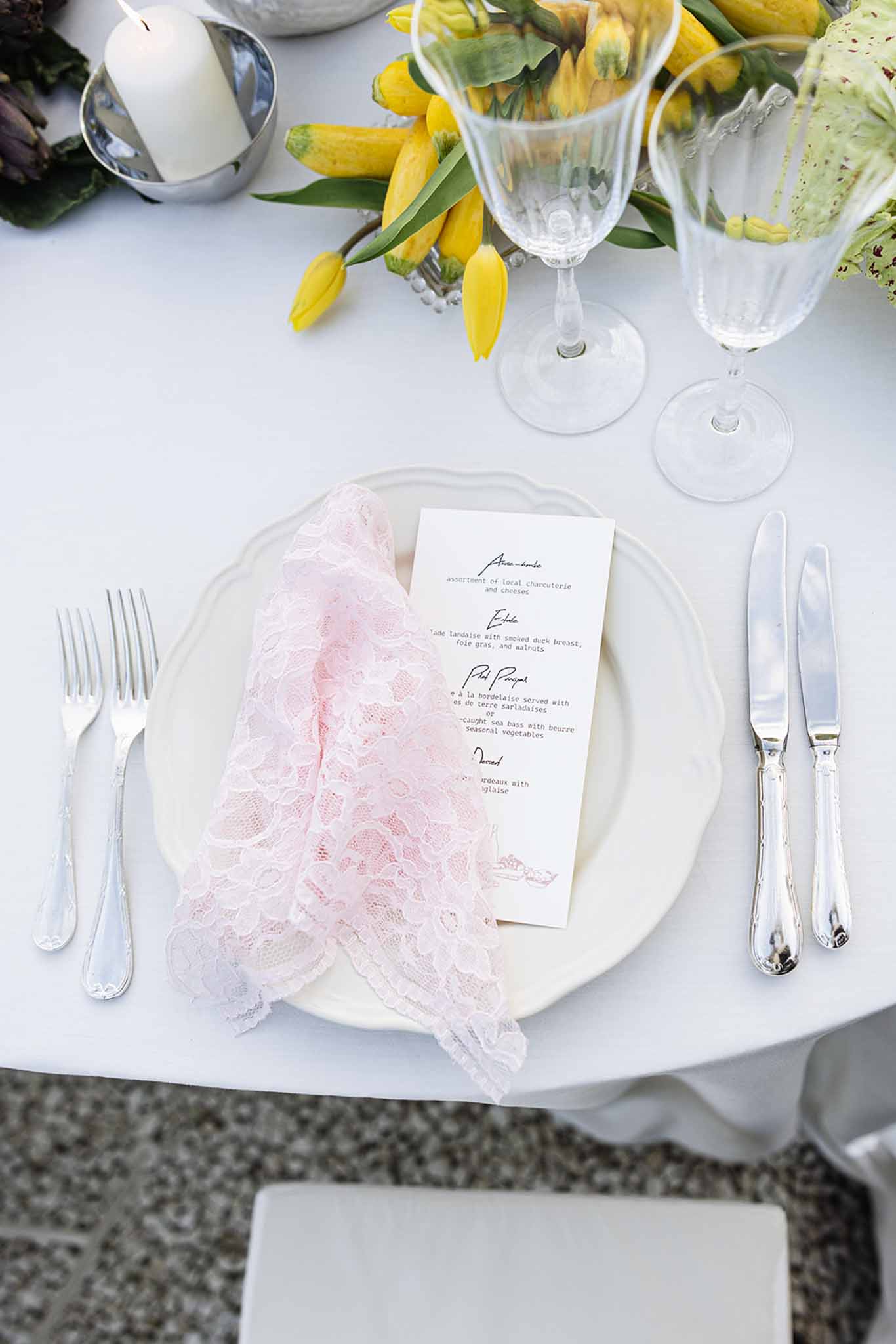 Overhead flat lay of elegant wedding reception place setting with blush napkin and yellow tulip centerpiece