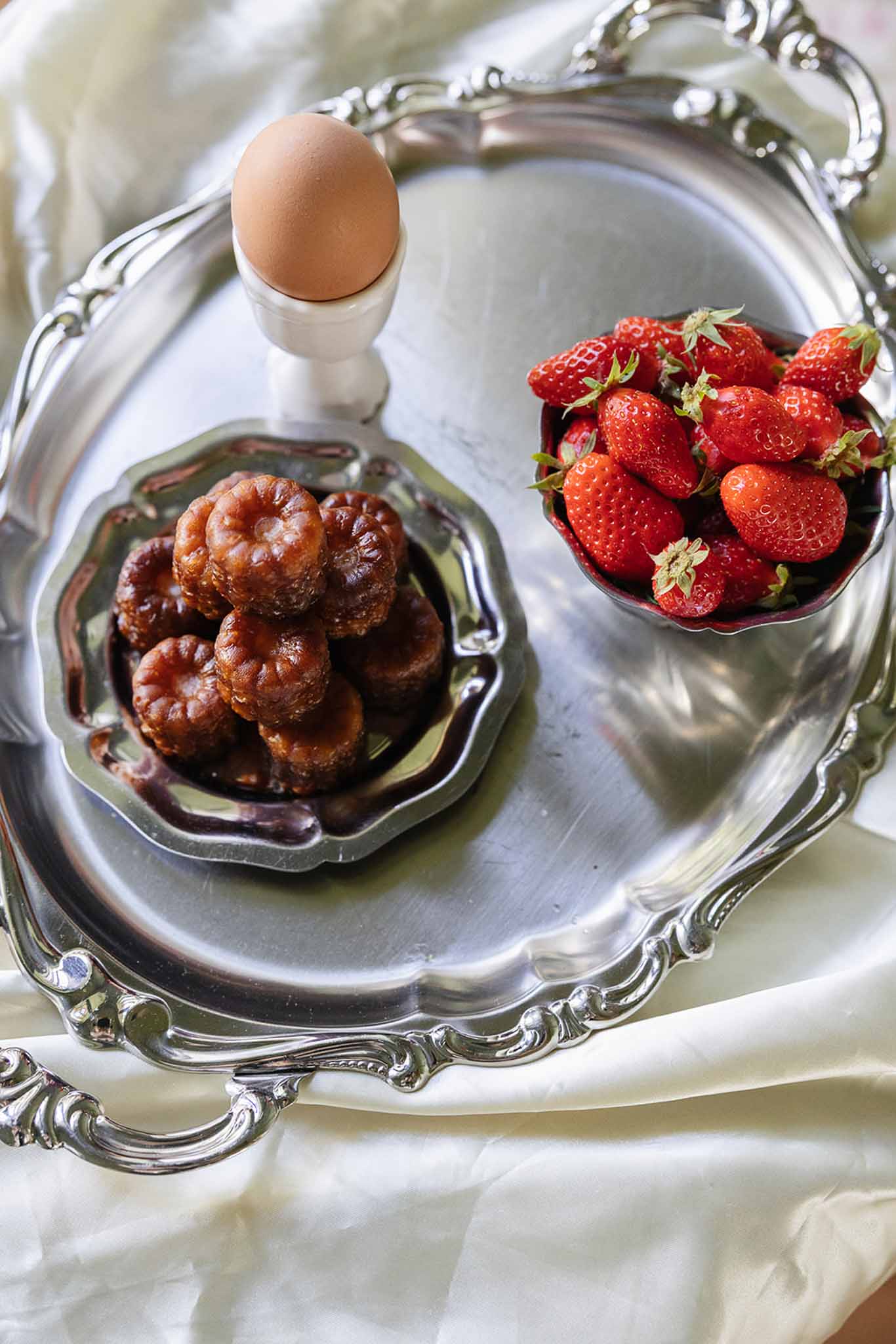Elegant breakfast flat lay with berries, egg and vintage silver platter on cream linens at wedding venue