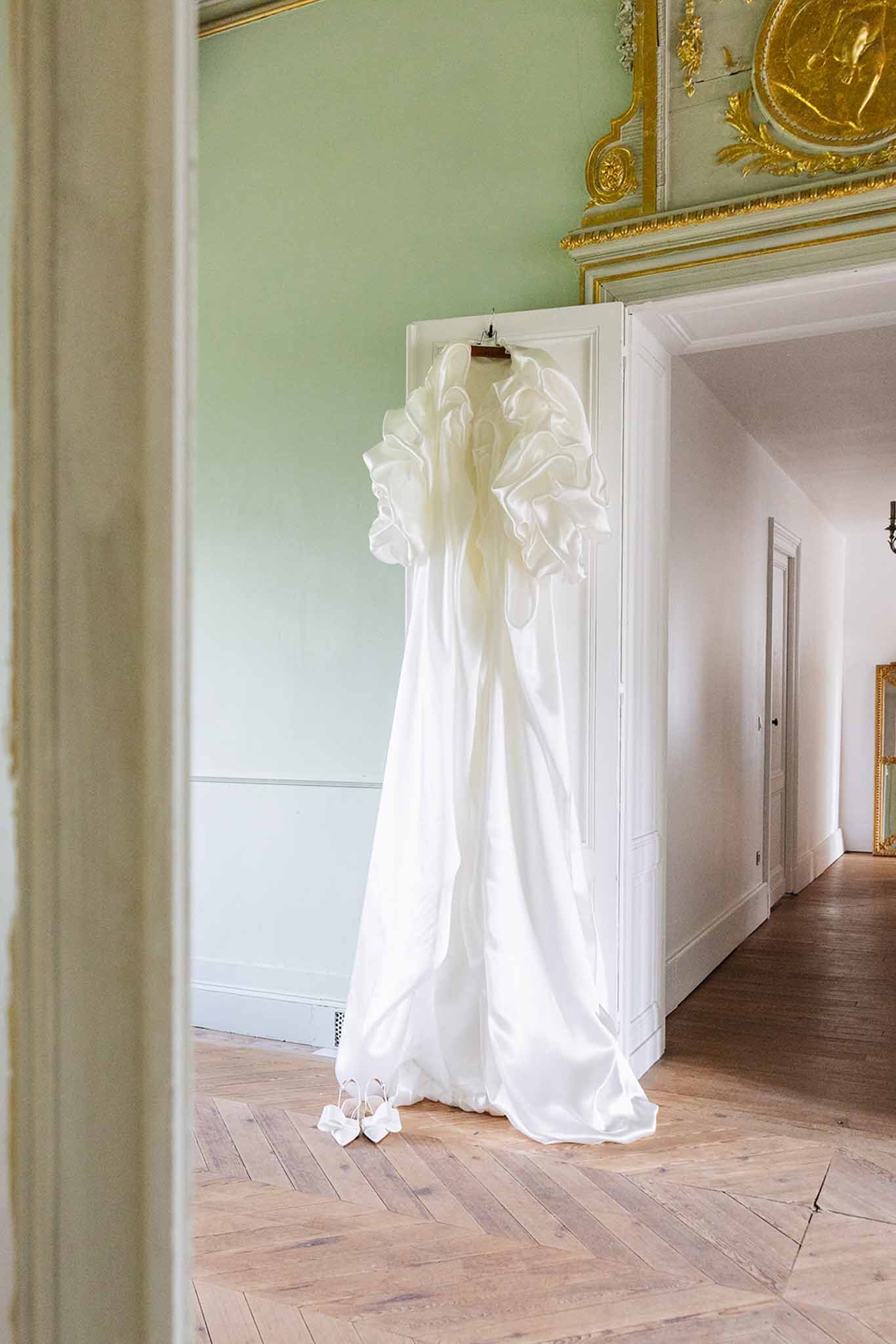 Ivory wedding dress hanging on door in classical château interior with herringbone floors