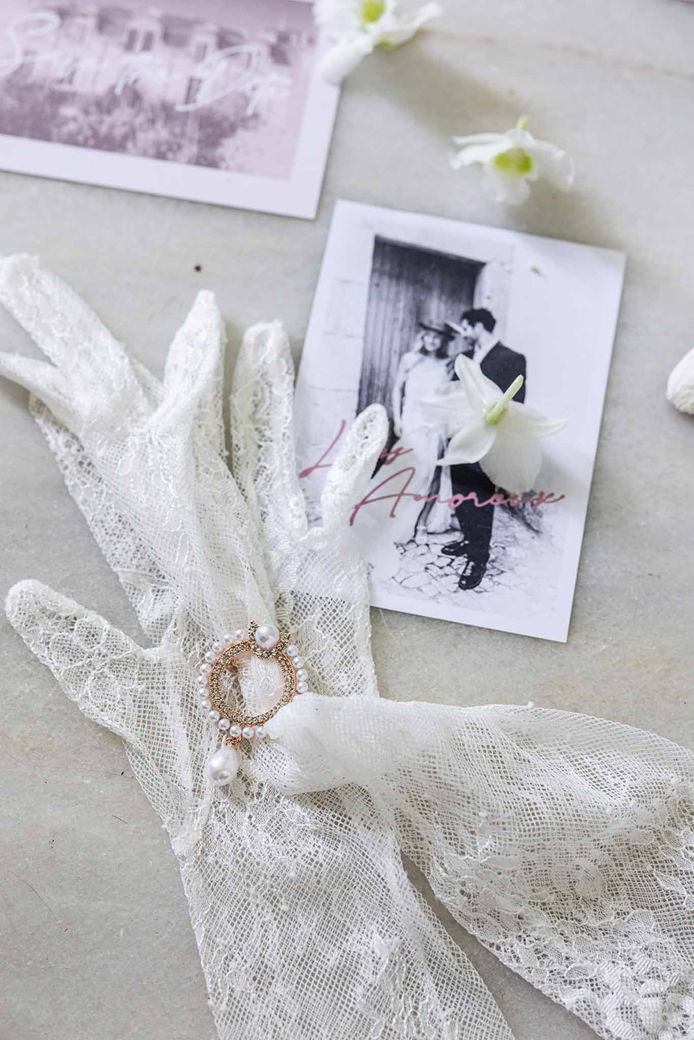 Wedding flat lay with black-and-white photos, ivory tulle veil, and gold jewelry on gray surface