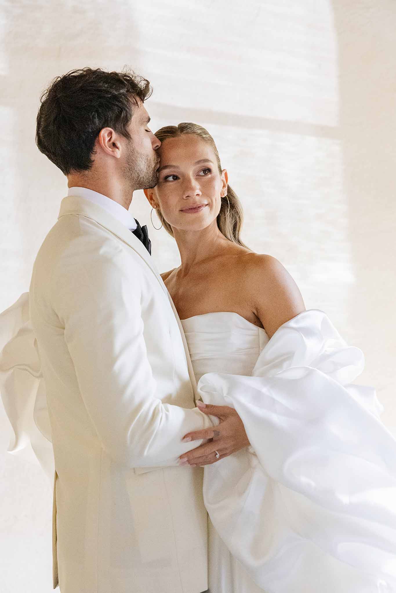 Intimate portrait of bride and groom with groom kissing bride's cheek in indoor setting