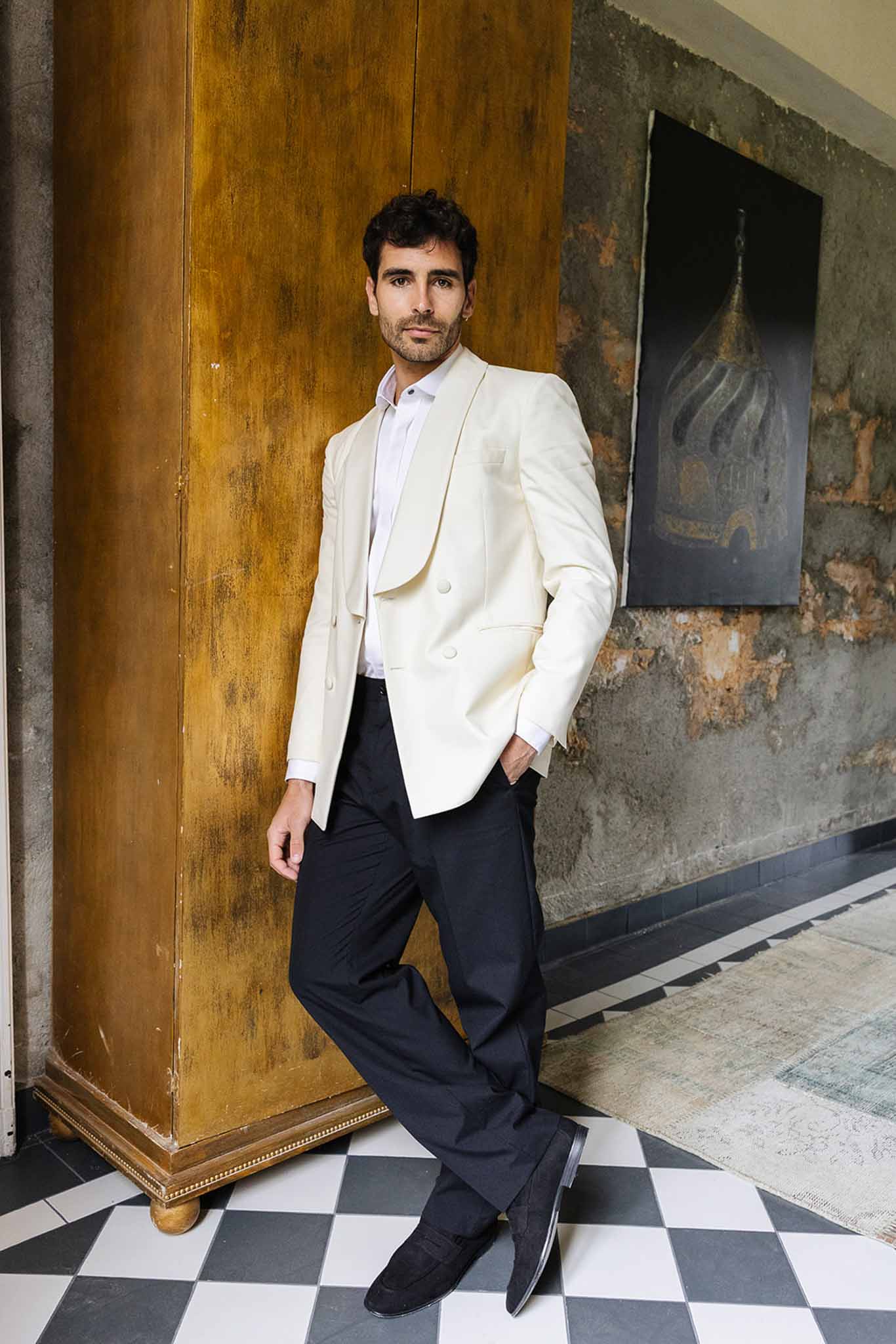 Groom in cream blazer and navy trousers posing in industrial venue with geometric floor