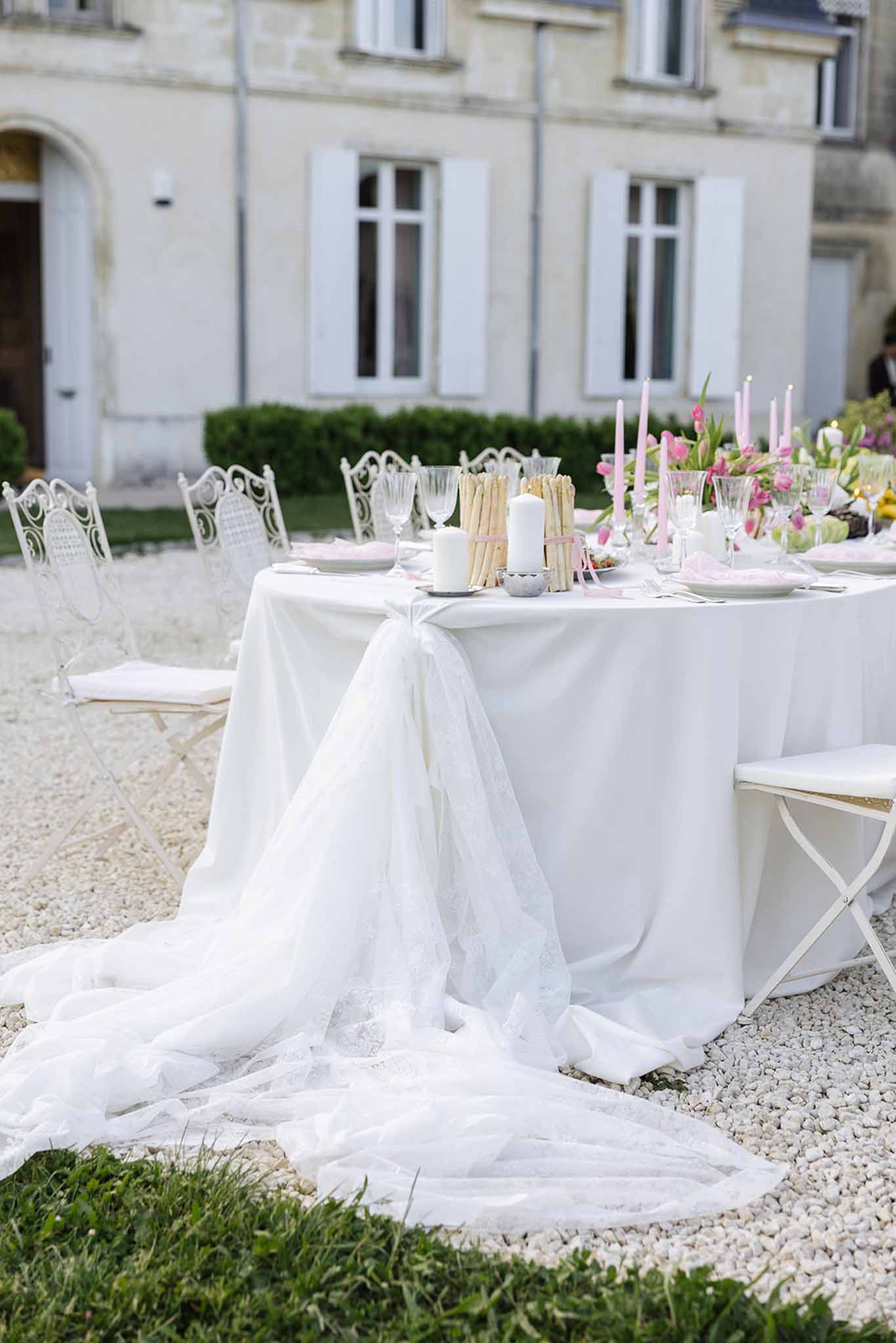 Elegant reception table setup with ivory linens and pink florals in outdoor courtyard with stone building