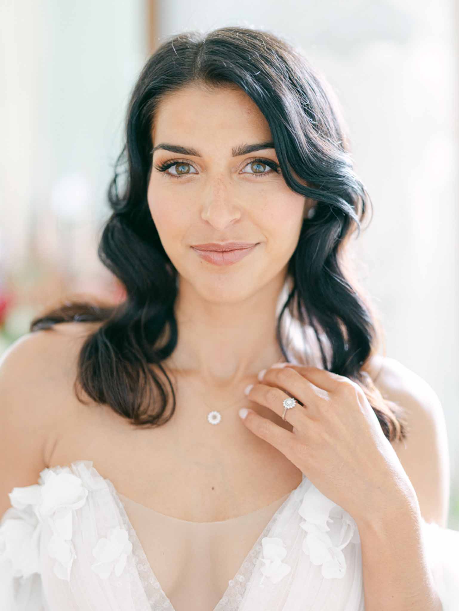 Close-up bridal portrait with dark wavy hair wearing V-neckline gown with floral applique and diamond necklace