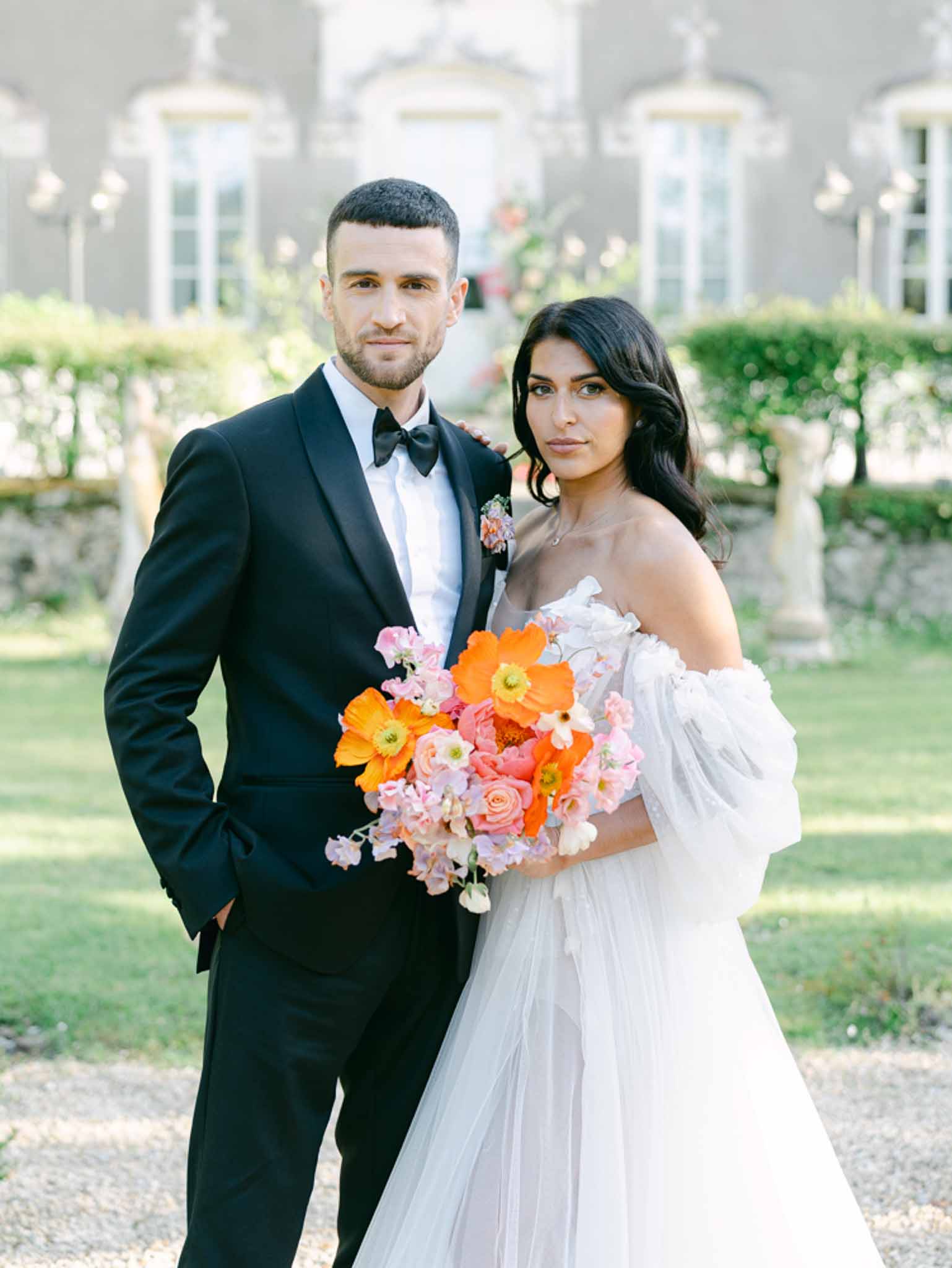 Couple portrait at chateau with bride holding bold orange poppy and coral ranunculus bouquet