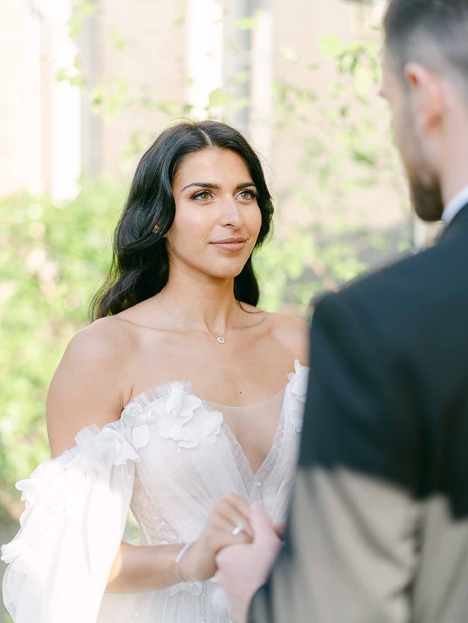 Bride in off-shoulder floral applique gown looking at groom during outdoor ceremony