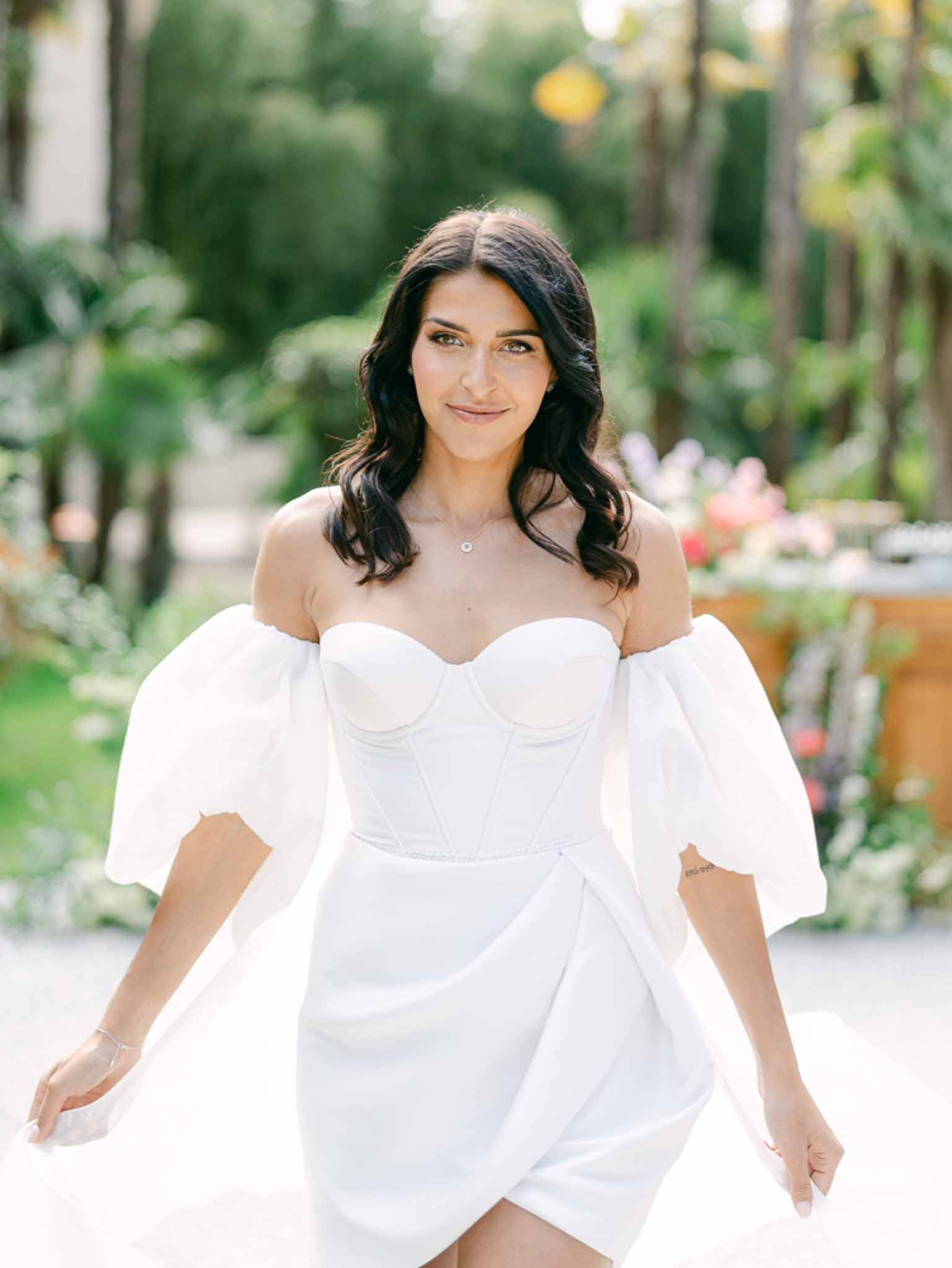 Bride in white off-shoulder mini dress with puff sleeves and diamond pendant in garden setting