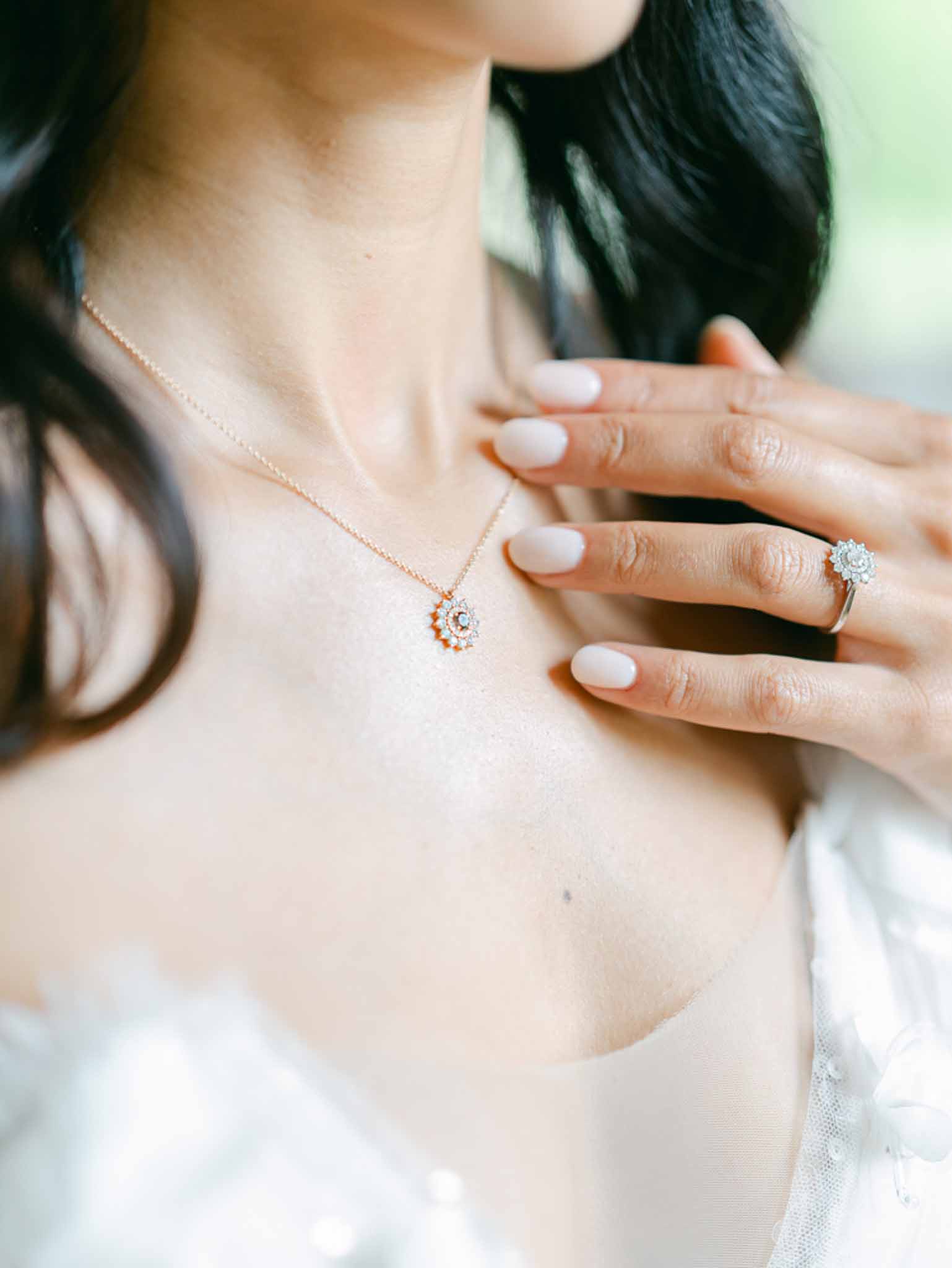 Close-up of bride's rose gold sunburst necklace and halo diamond engagement ring