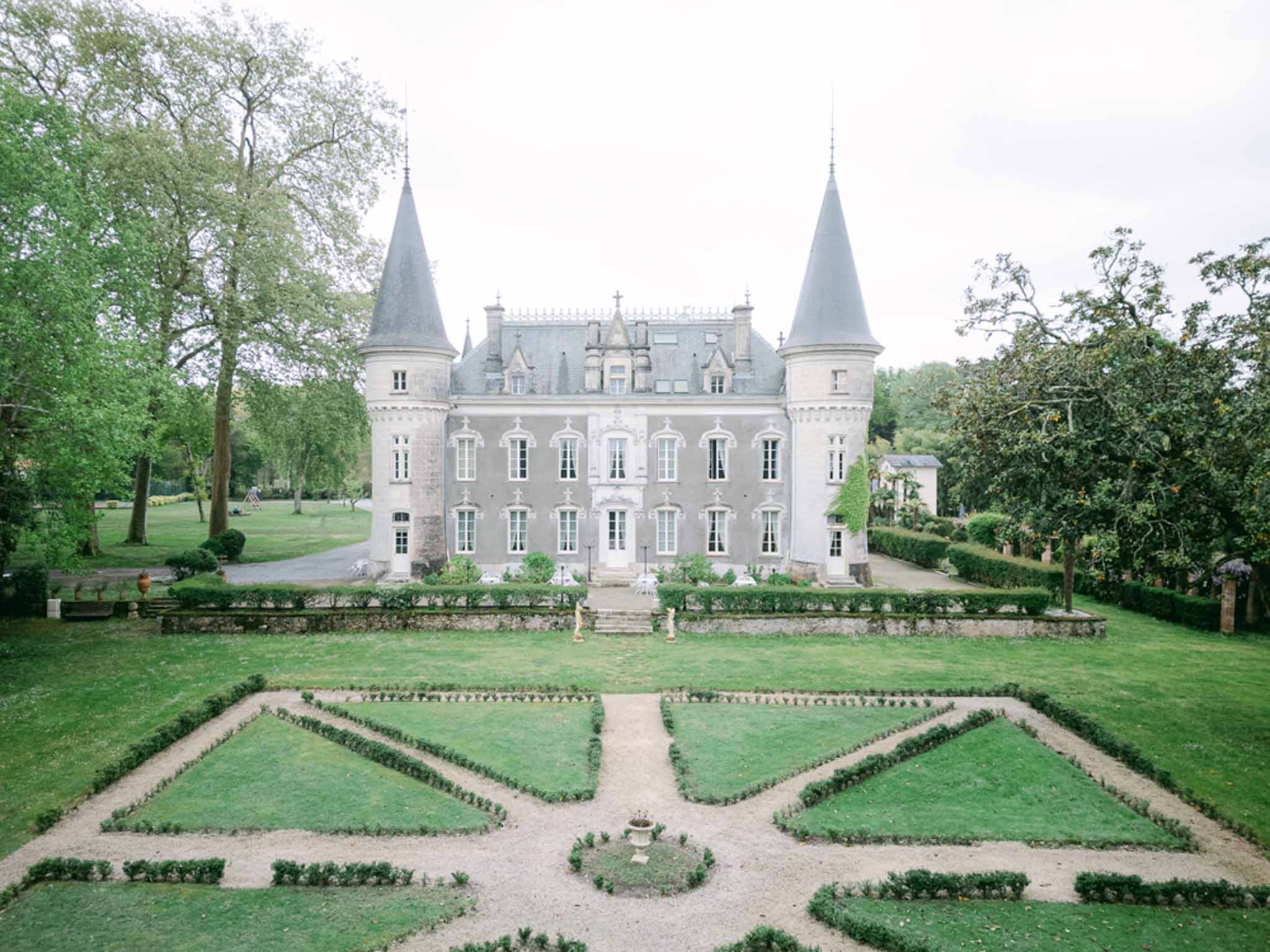 Chateau with pointed turrets, boxwood parterre garden, and ceremony chairs on gravel forecourt