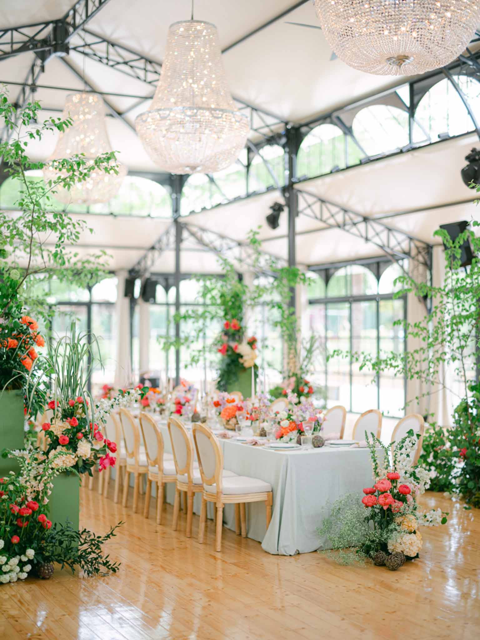 Greenhouse reception table with coral ranunculus and lavender centerpieces, crystal chandeliers, and sage linen