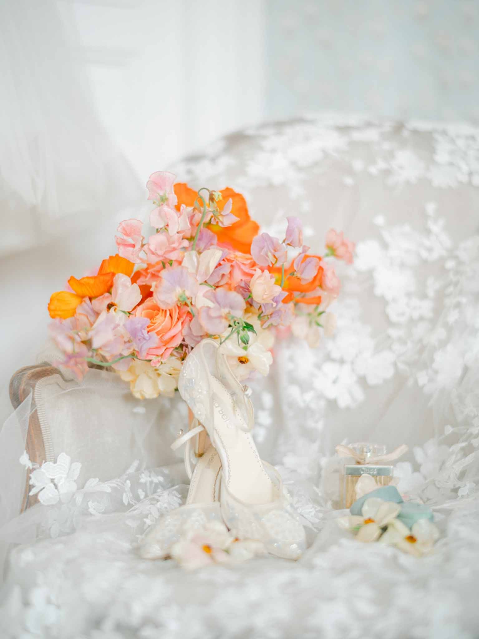Orange poppy and peach rose bouquet with lace bridal heels and floral-applique gown on cream surface