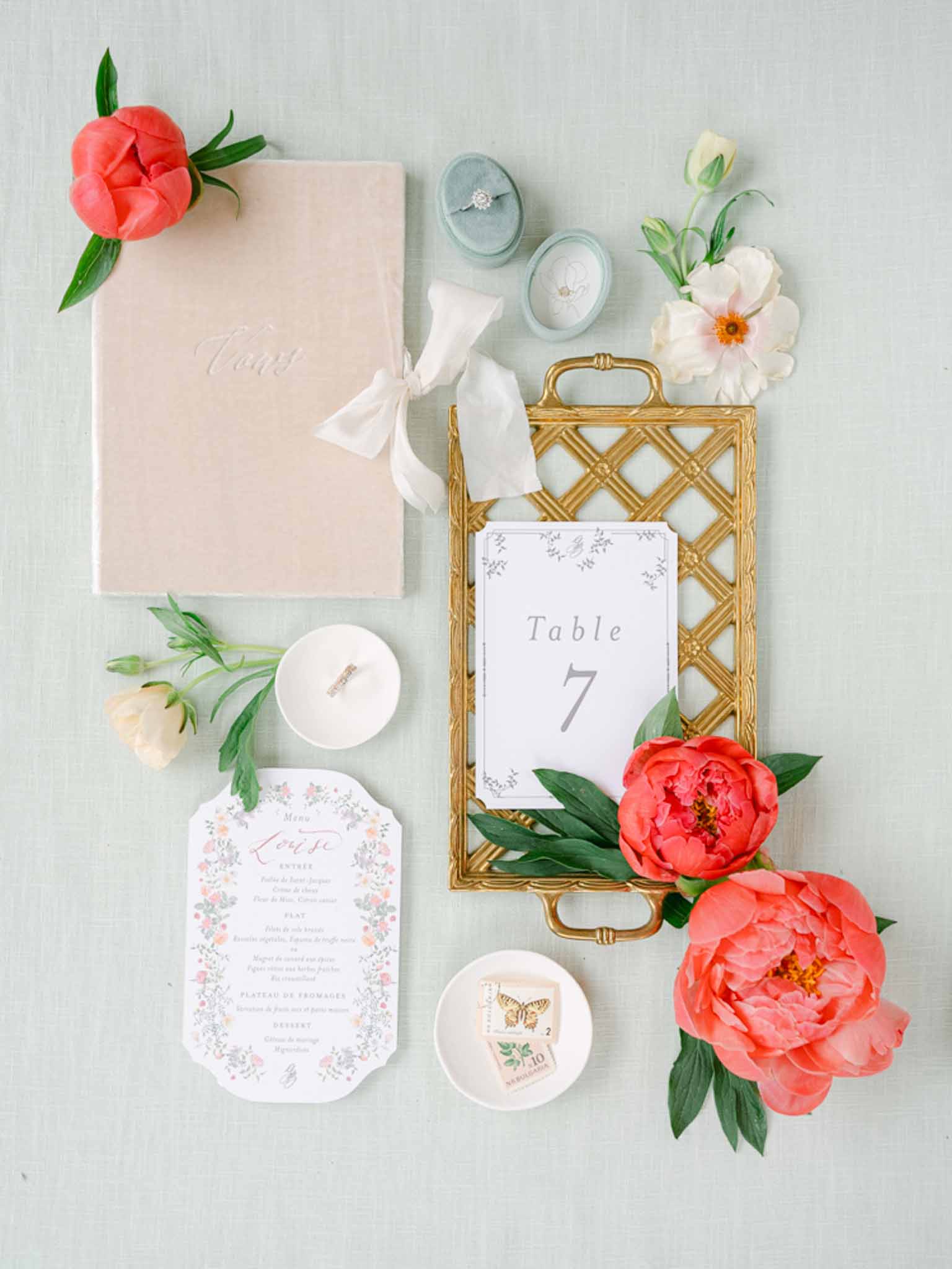 Stationery flat lay on sage linen with coral peonies blush toast book floral menu card blue velvet ring boxes and gold tray