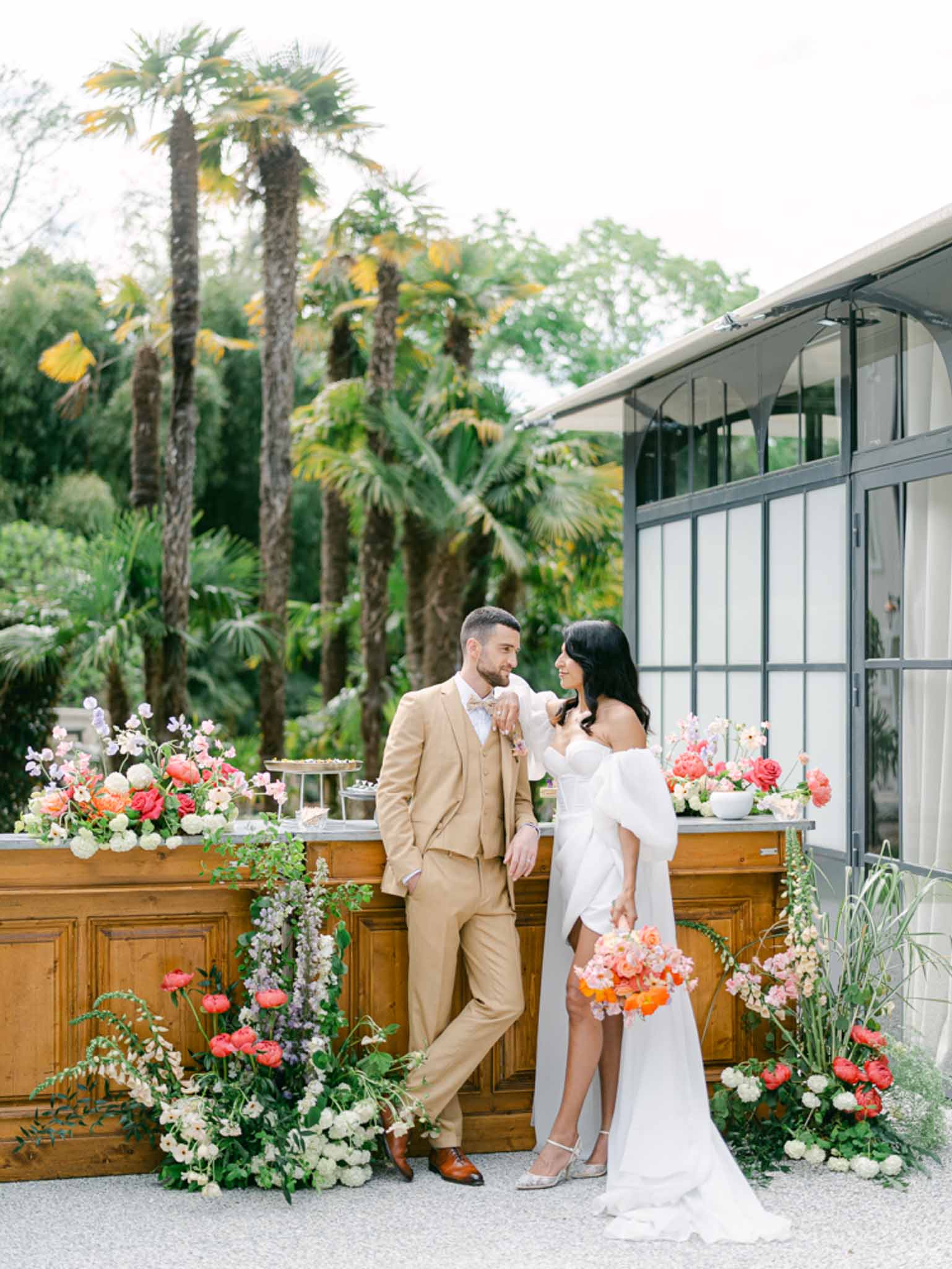Couple posing at wooden bar decorated with coral ranunculus and wisteria at greenhouse venue