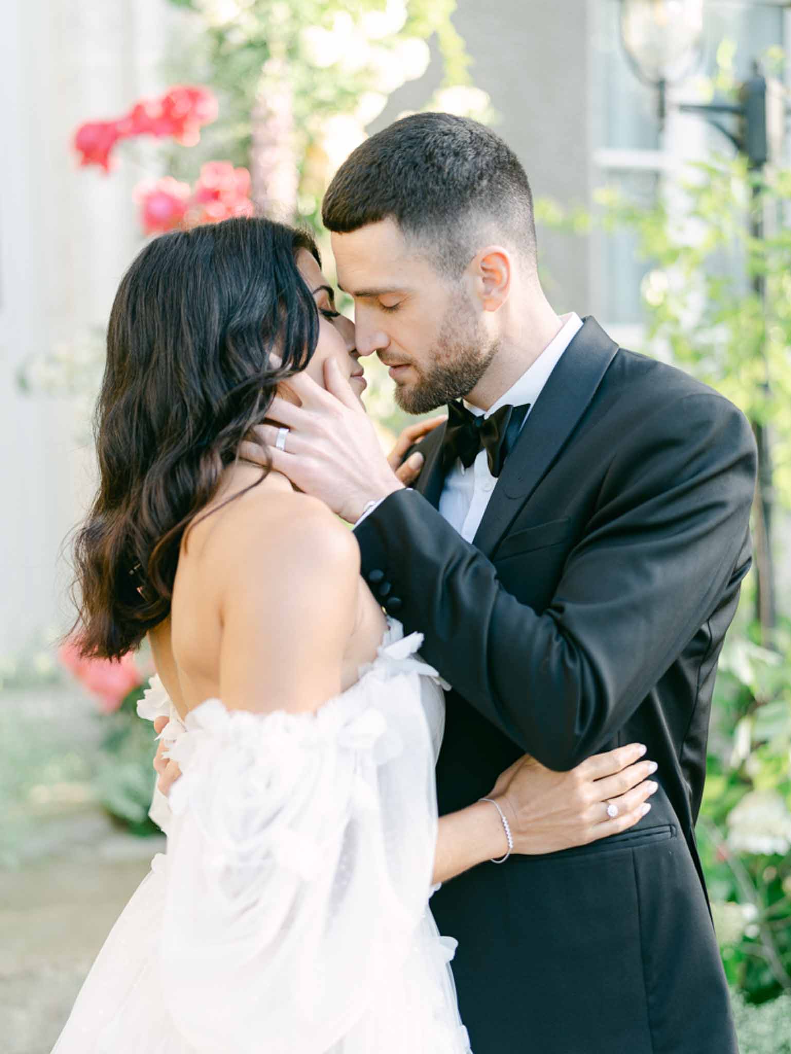 Close-up of couple leaning foreheads together before columned facade with coral climbing roses