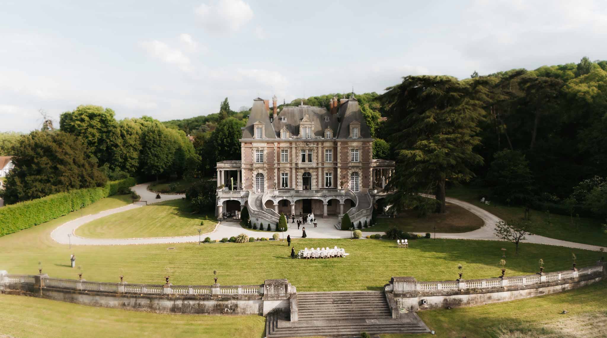 Aerial view of 19th-century brick and stone chateau with curved staircase and lawn table setup