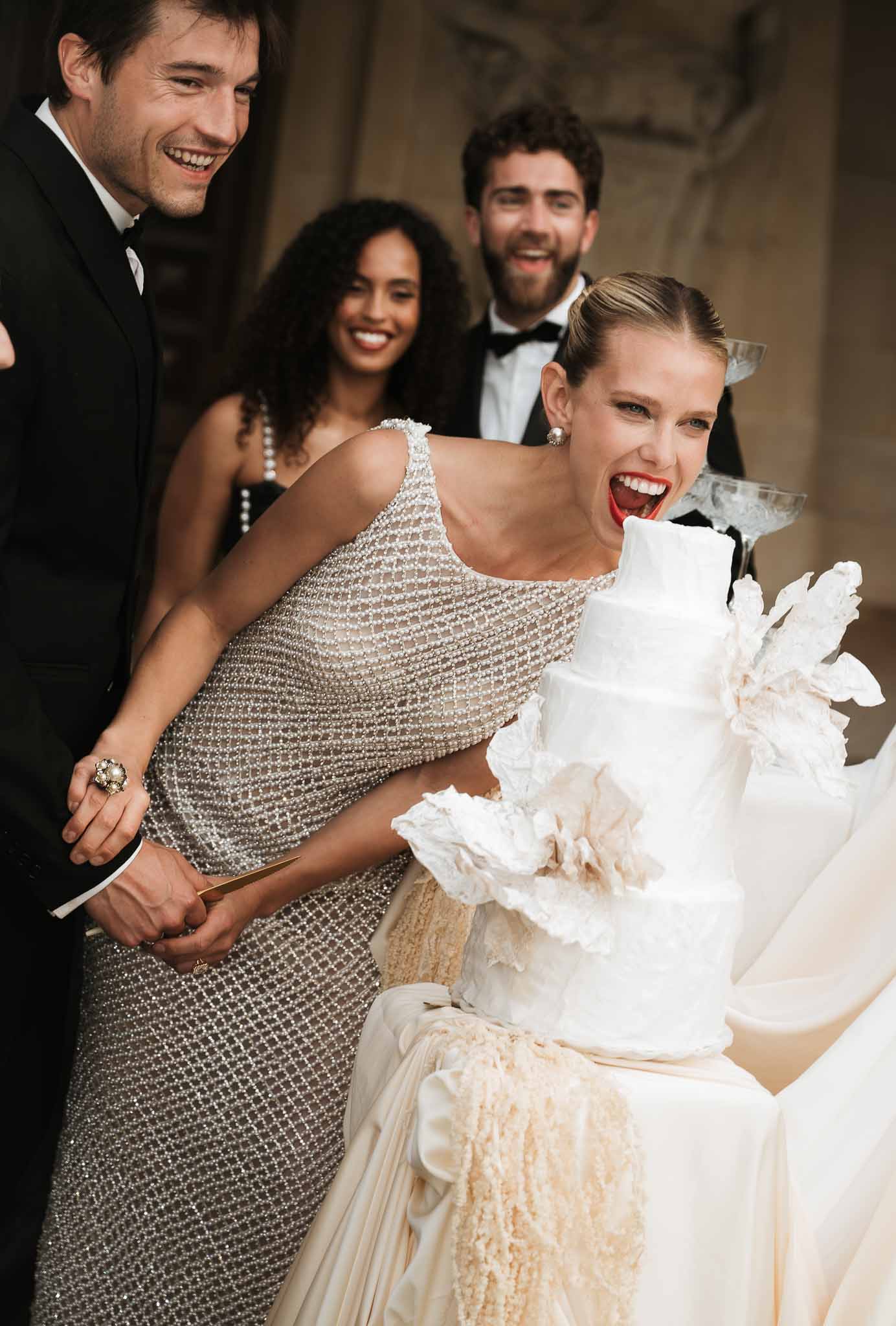 Bride in silver sequin gown and groom cutting three-tier white sugar flower cake