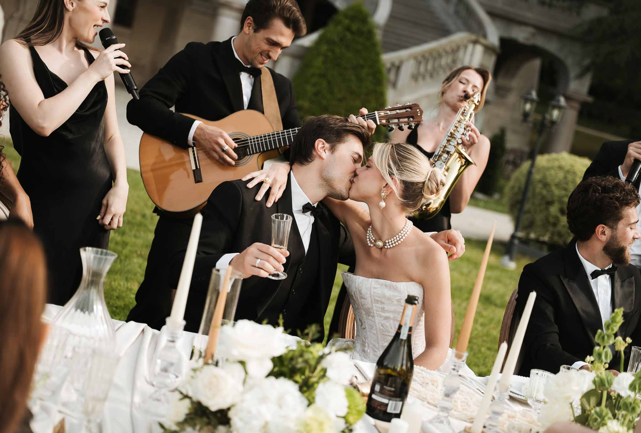 Bride and groom kiss at head table as three-piece band with vocalist and saxophonist perform behind