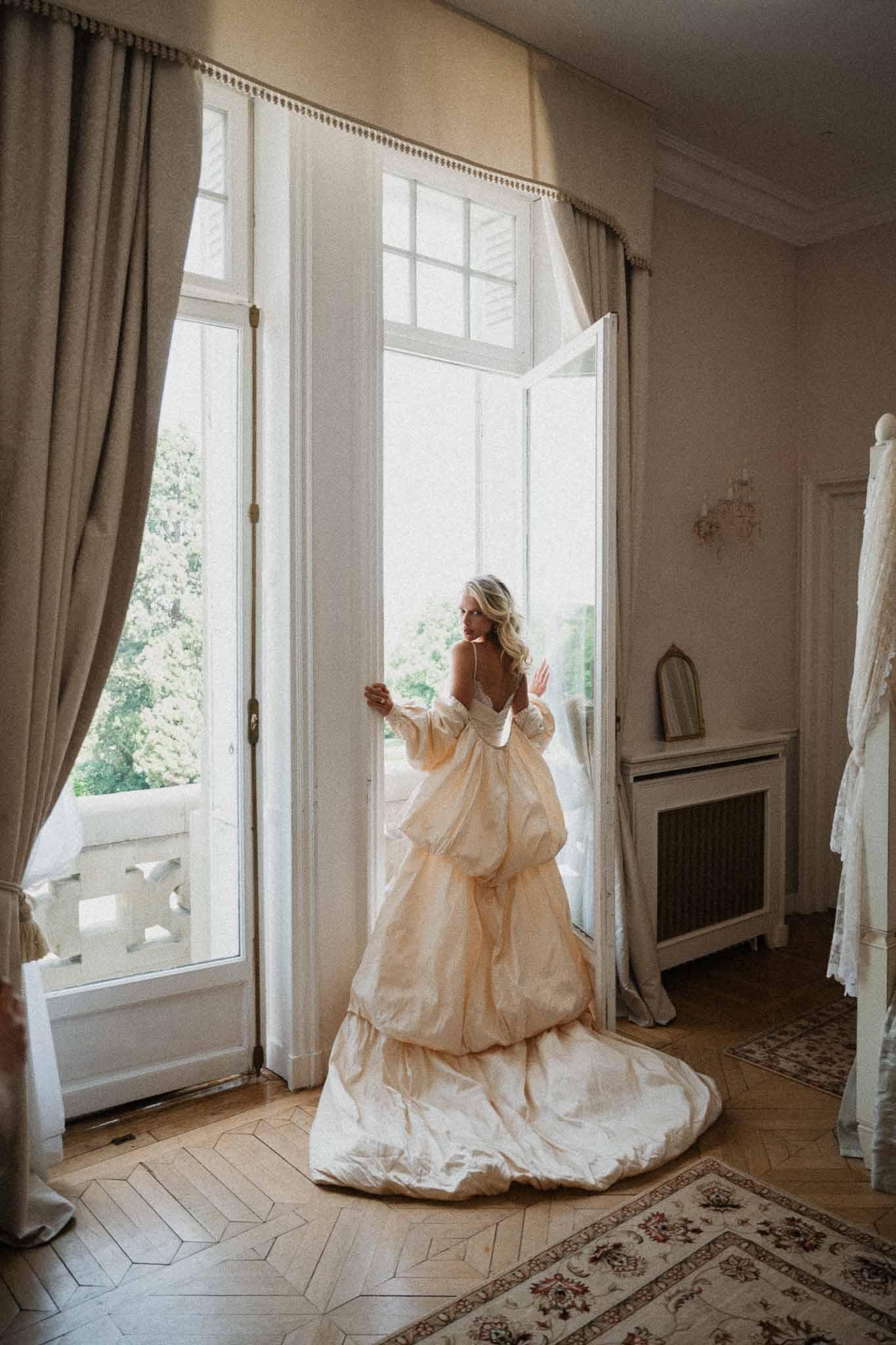 Bride from behind in champagne ballgown with puffed sleeves opening French doors in chateau room