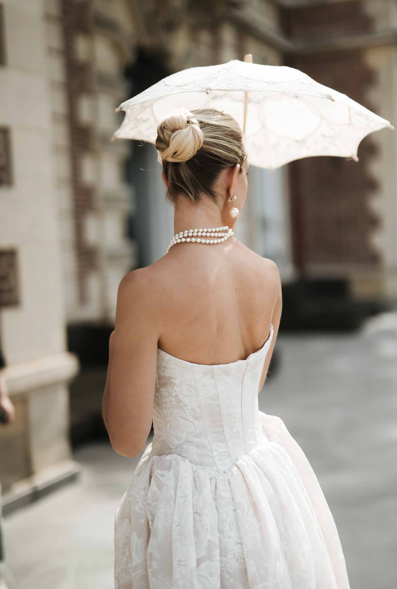 Bride from behind in strapless ivory brocade ballgown with lace parasol and pearl choker in sleek high bun