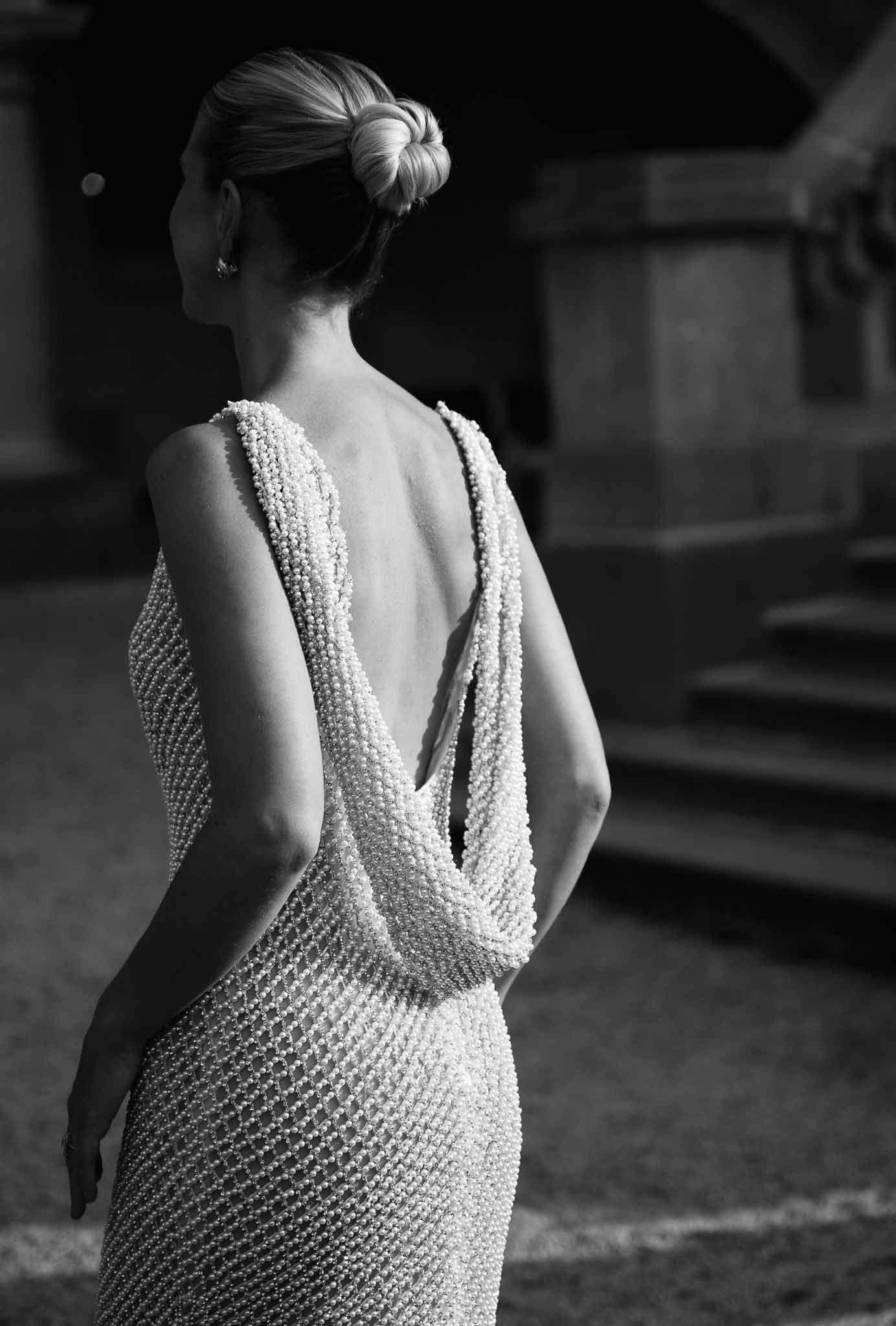 Black and white close-up of open-back pearl-beaded gown with draped pearl strands and low twisted bun from behind