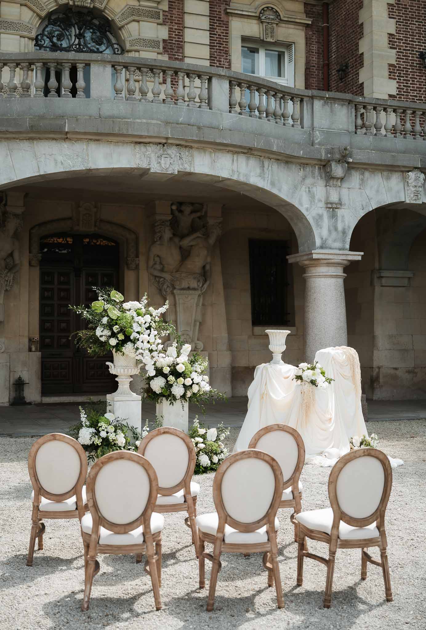 White hydrangea urns and draped altar before ornate red brick chateau facade with carved sculptures