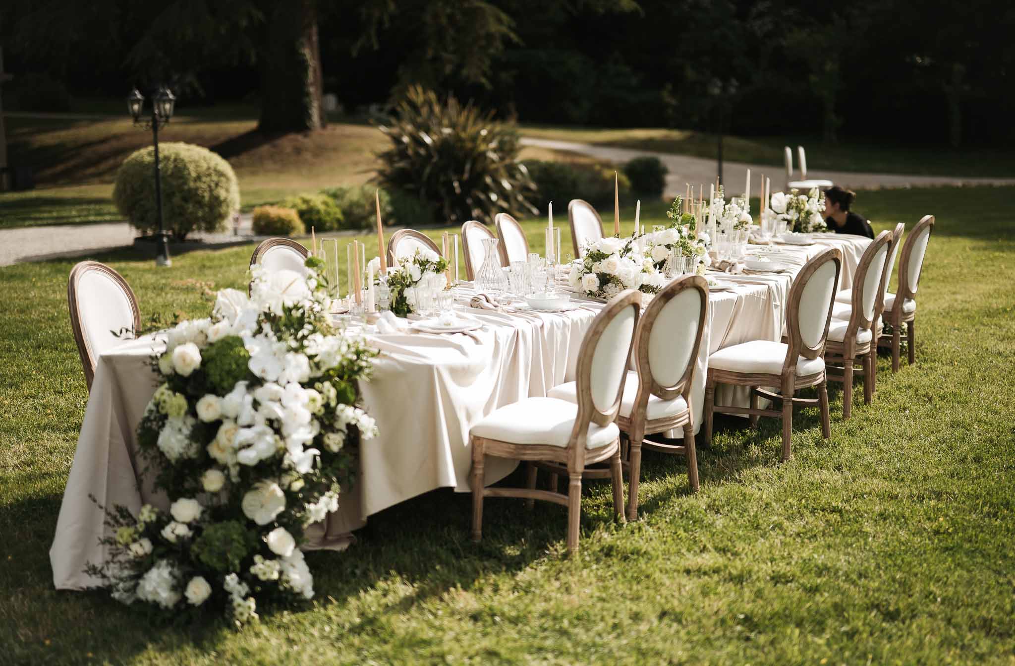 Long table with cascading white roses and orchids, ivory tapers, and Louis XVI chairs on manicured lawn
