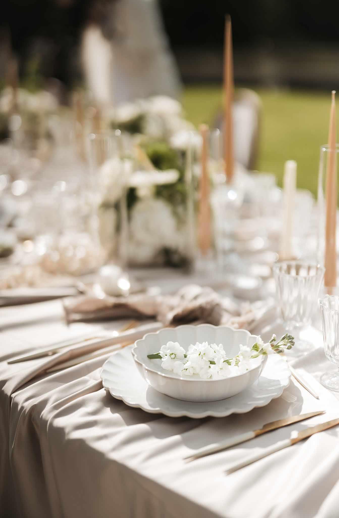 Minimalist place setting with scallop-edged bowl, gold flatware, and gold taper candles on ivory linen