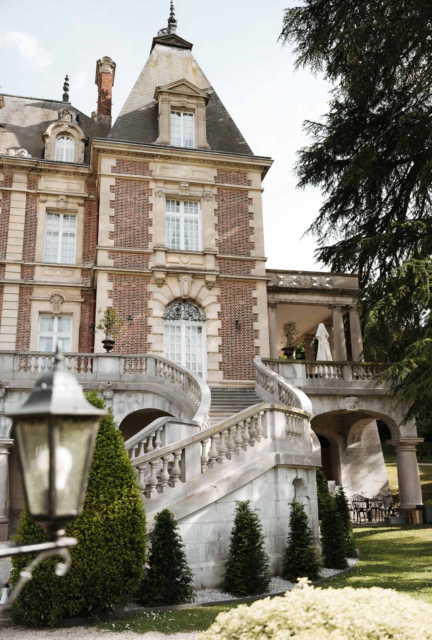 Red brick and cream stone Second Empire chateau with horseshoe staircase conical topiary and ironwork