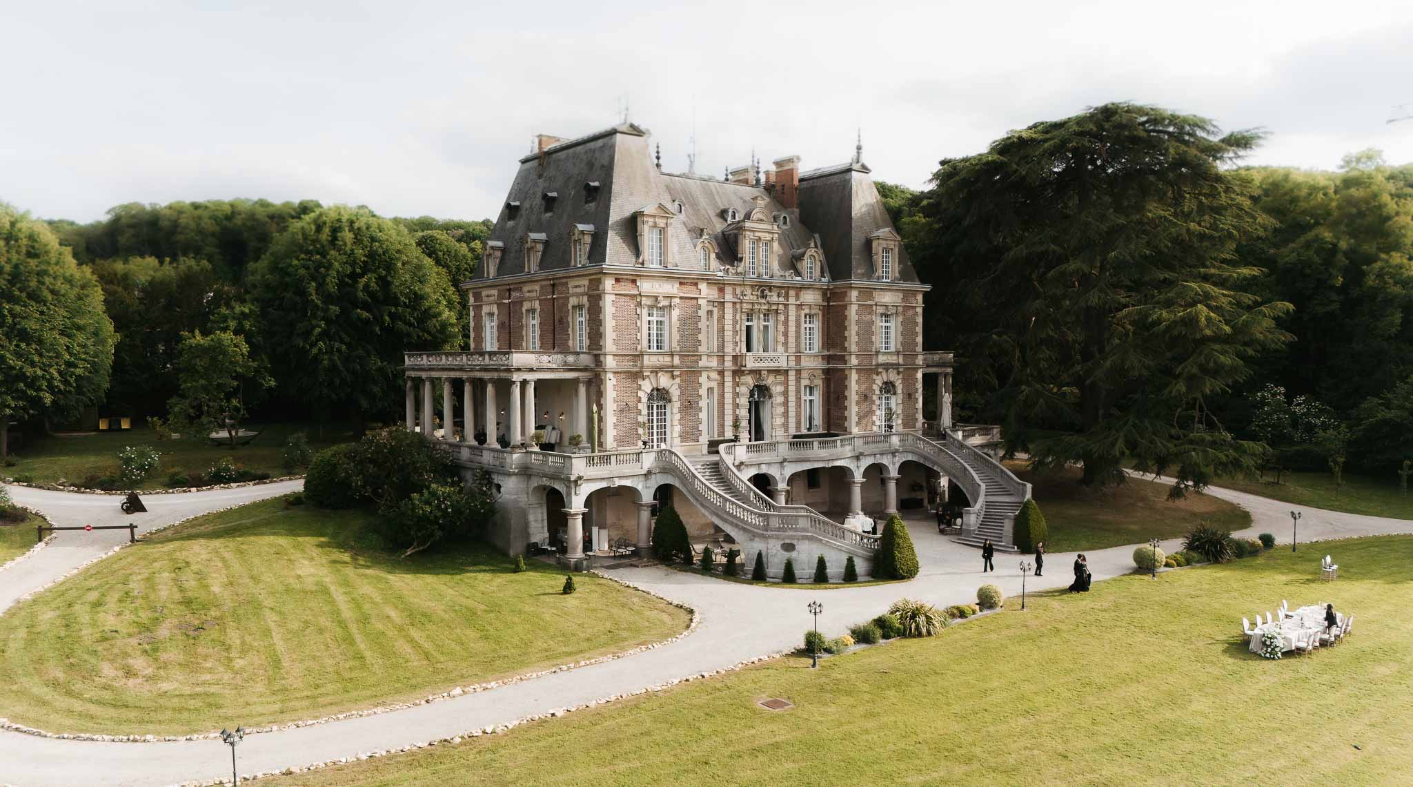 Aerial 19th-century brick-and-stone chateau with mansard roof double horseshoe staircase and colonnaded terrace